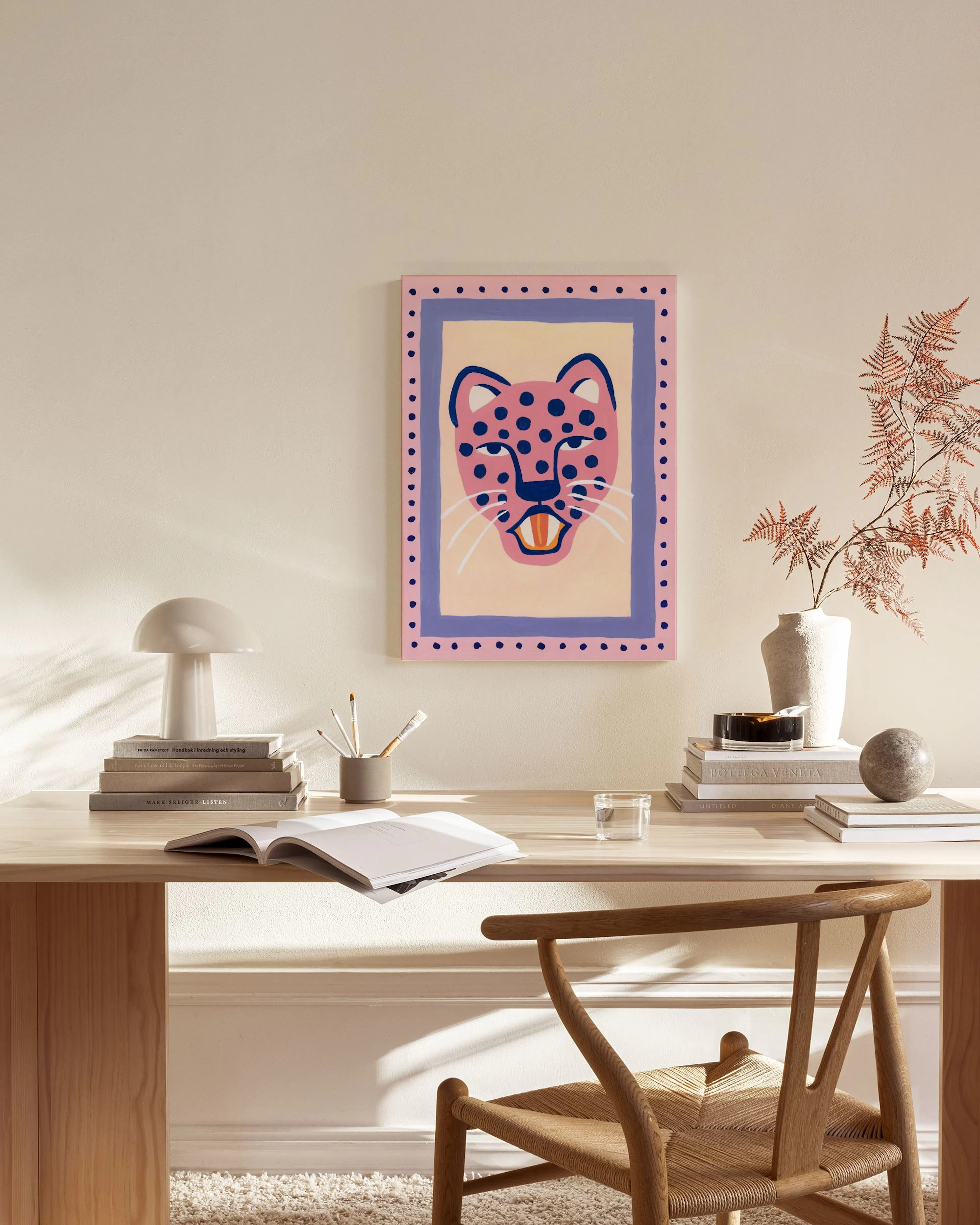 A vibrant pink leopard face with blue spots and white whiskers, hanging above a wooden console table in a minimalist living room