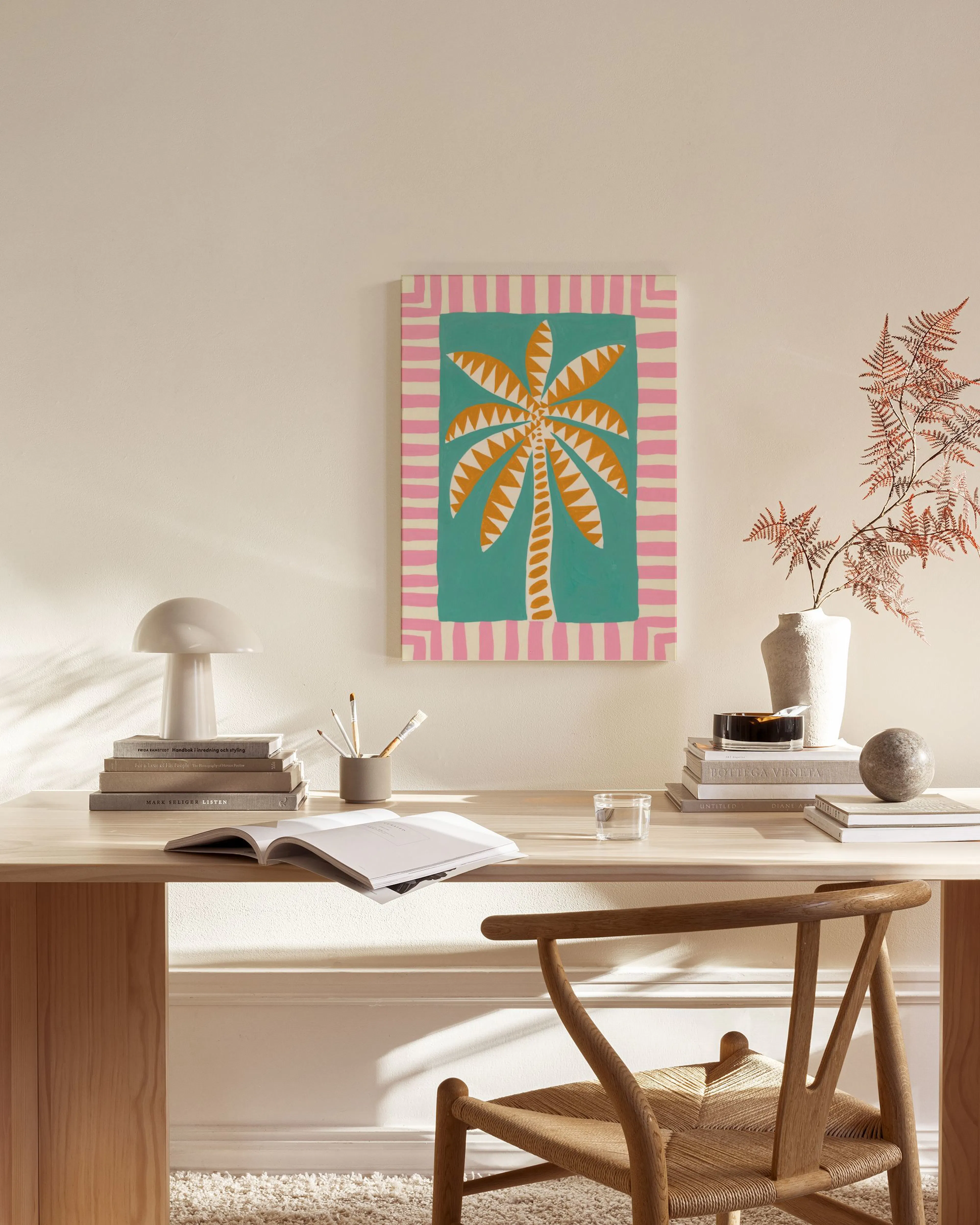 Stylised palm tree canvas print in orange and green on a pink striped background, displayed in a bright living room.