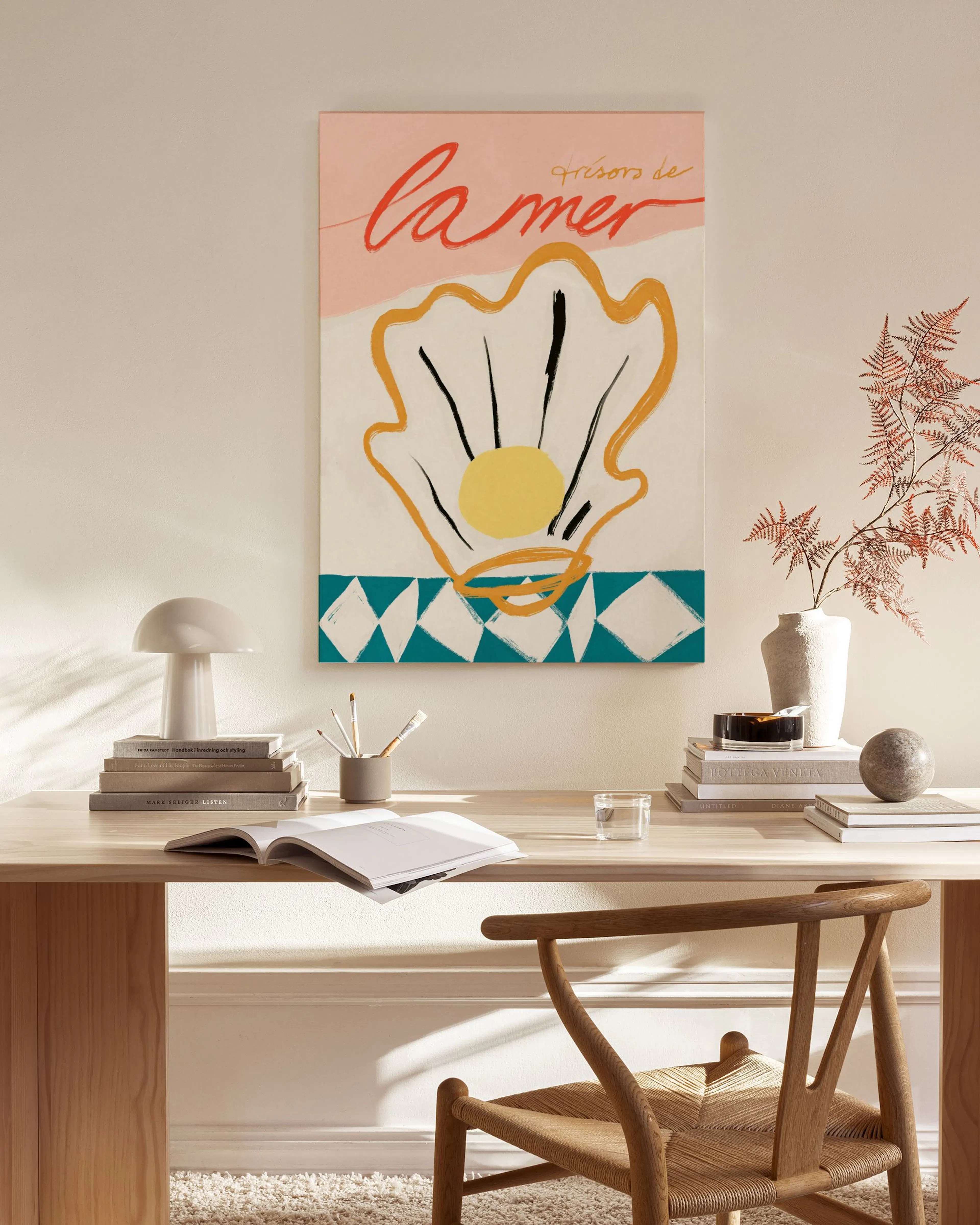 Lienzo con ilustración de concha de perla amarilla y ondas sobre fondo rosa y blanco, colgado sobre un mueble auxiliar de madera