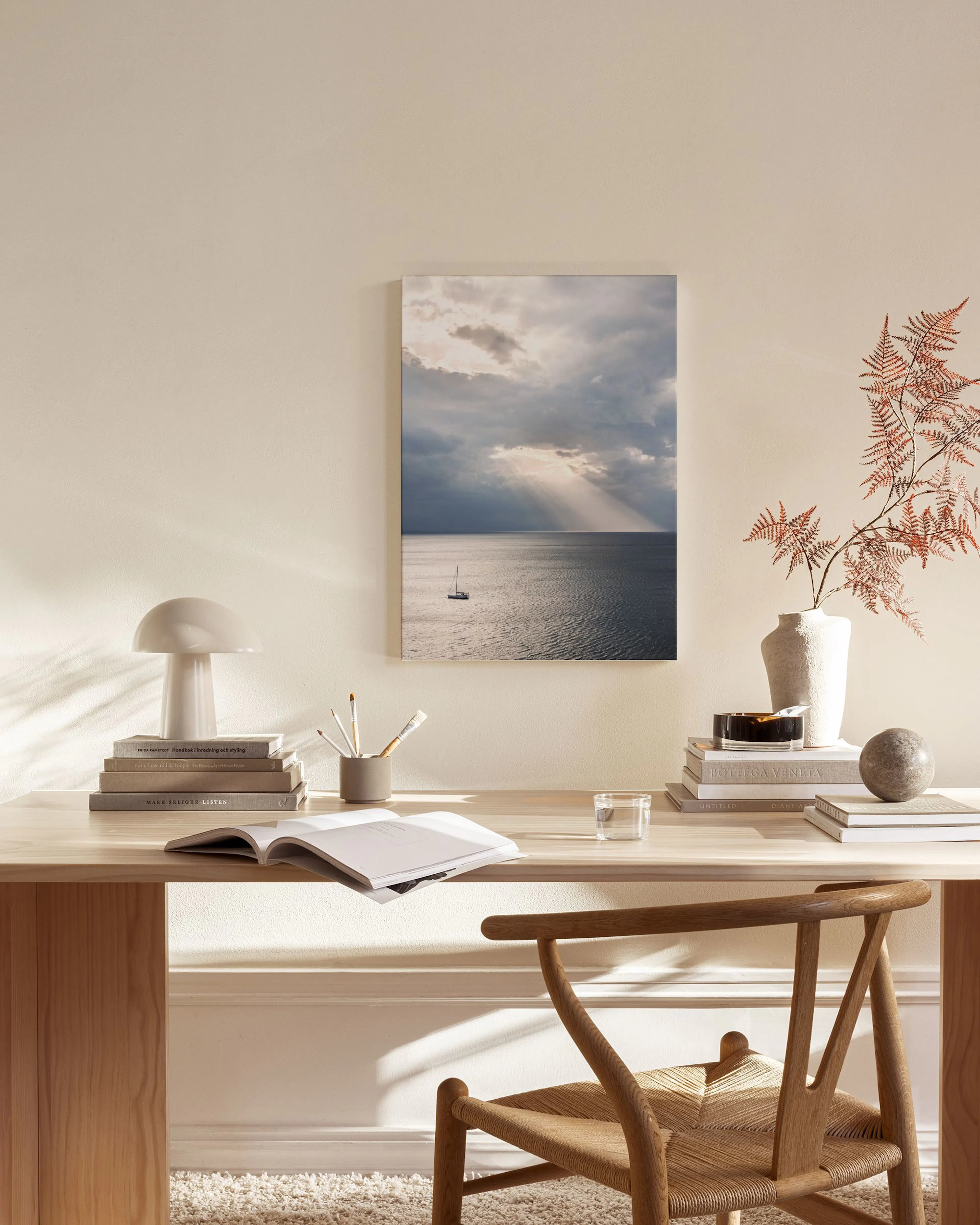 A canvas print of a sailboat in open water under a dramatic cloudy sky with sun rays, hanging in a minimalist living room.