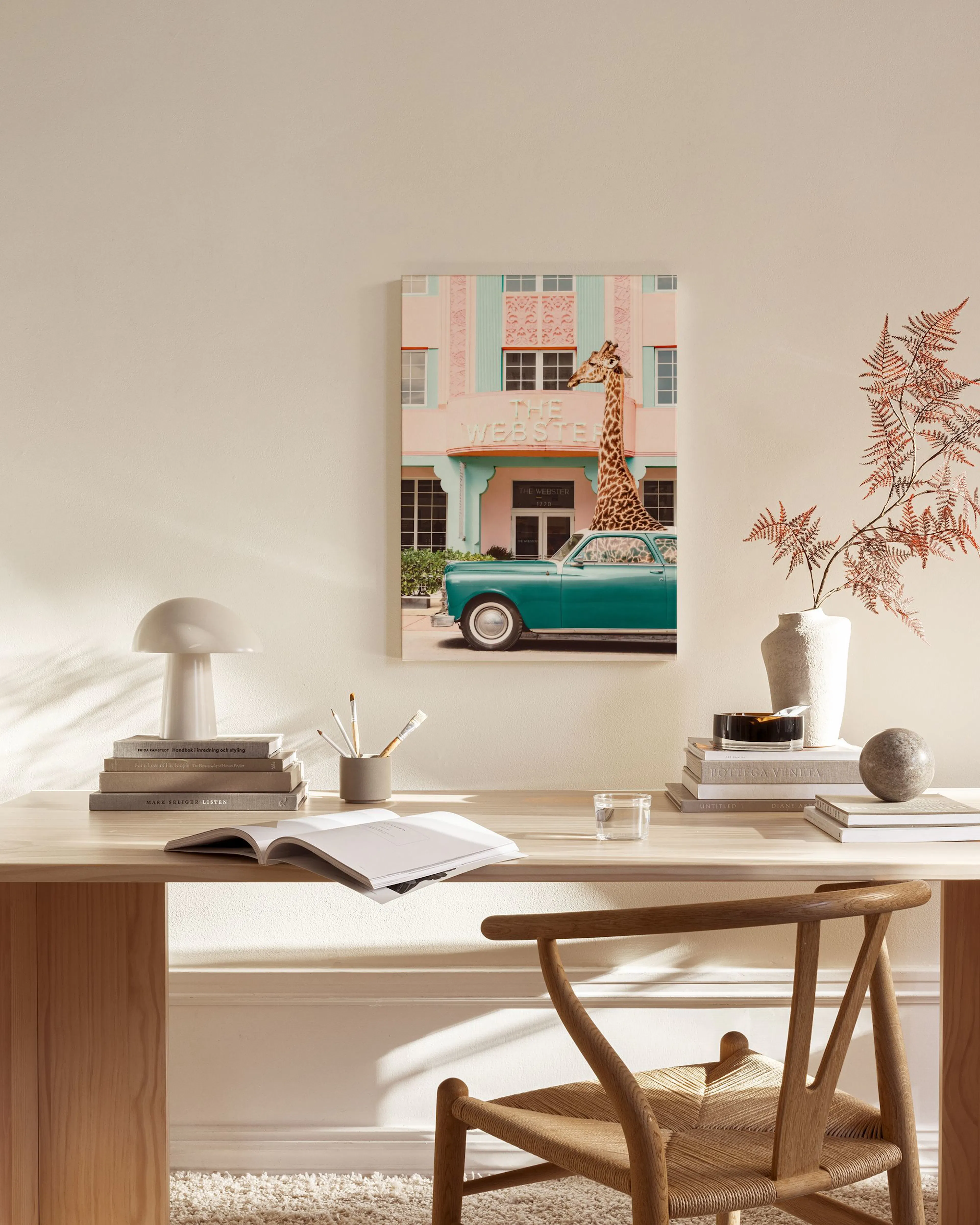Toile dune girafe sortant dune voiture turquoise devant une façade rose et bleue, accrochée dans un salon moderne.