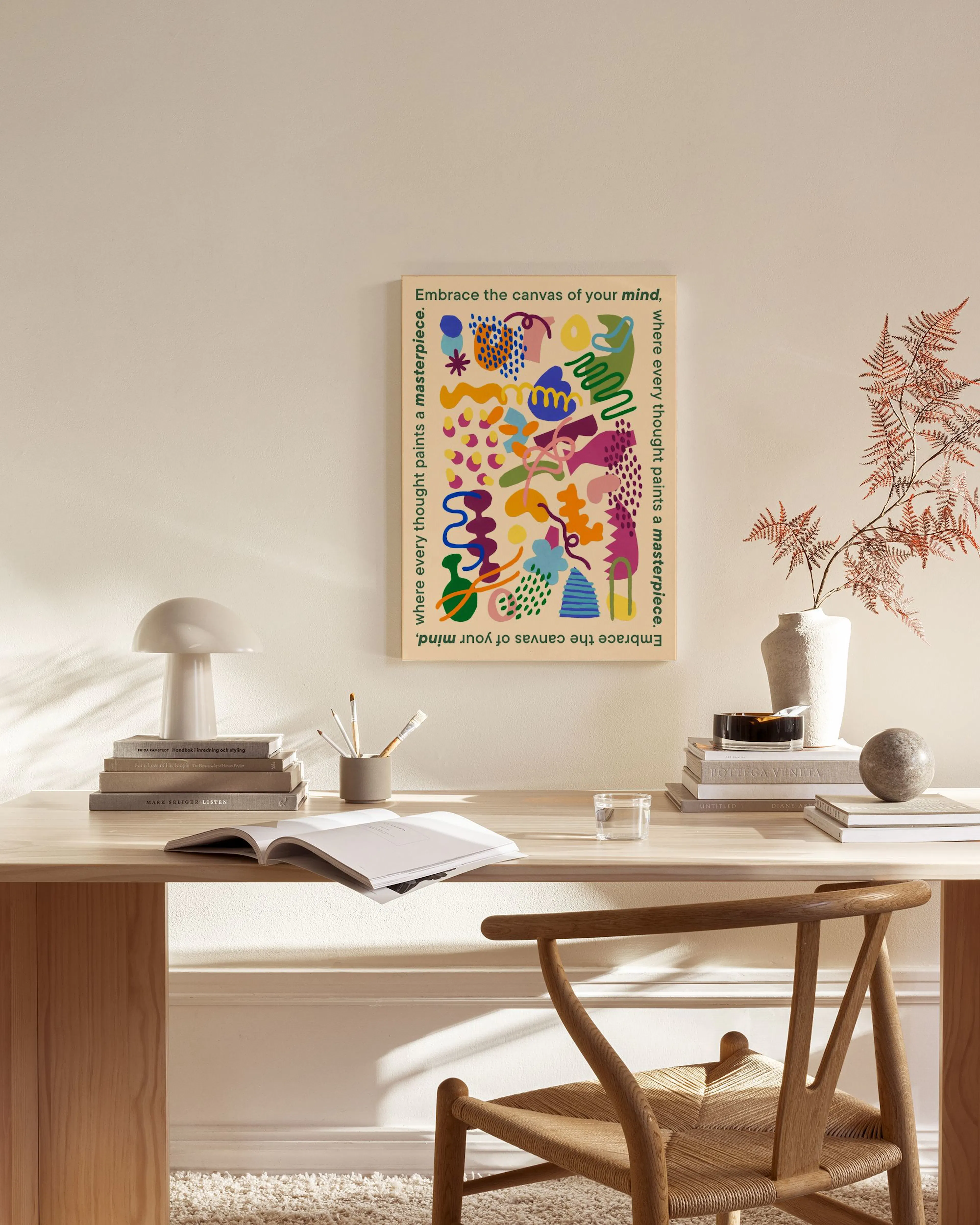 Lienzo con formas orgánicas coloridas y texto inspirador, colgado sobre un mueble bajo en una sala moderna.