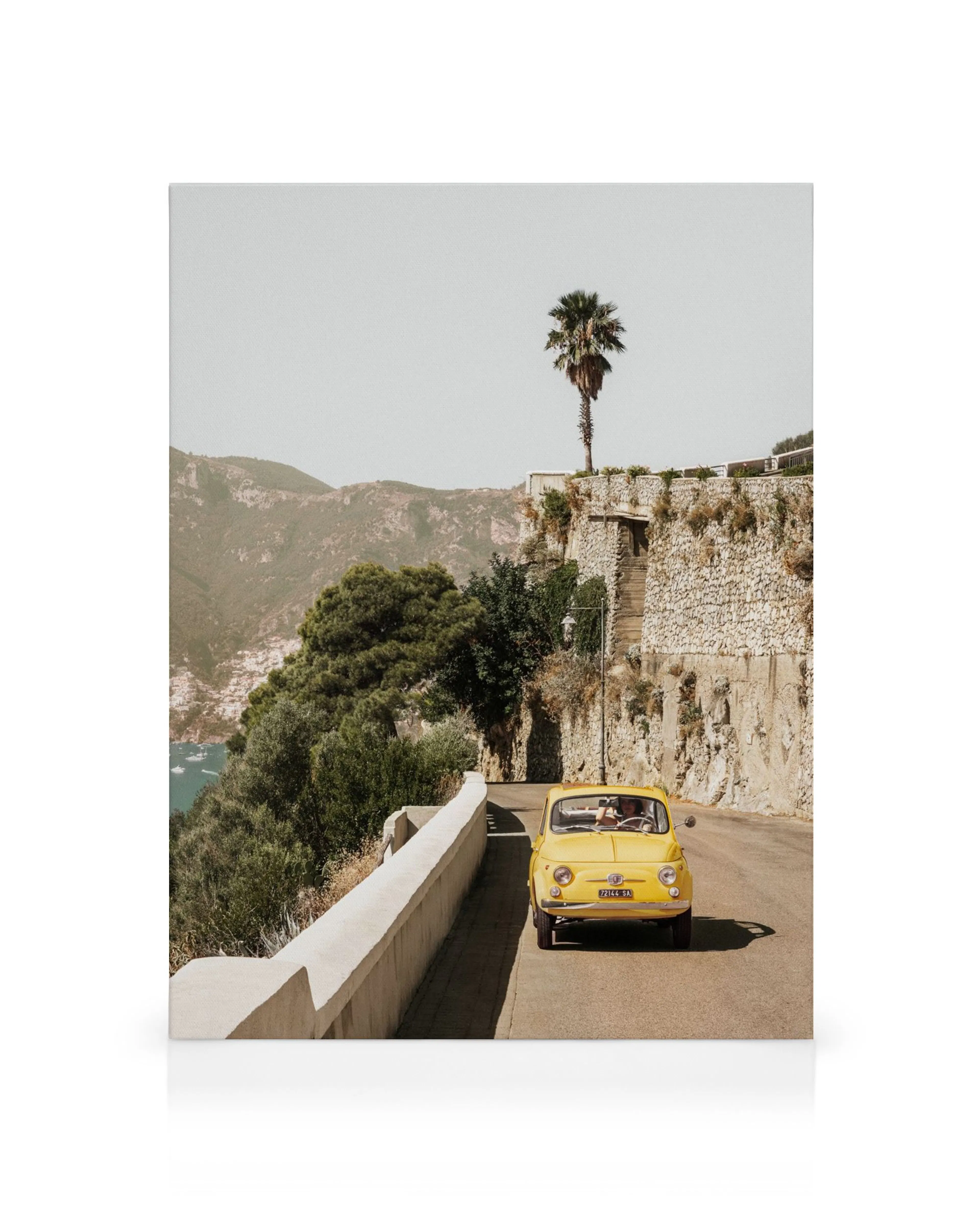 Fotografia di unauto depoca gialla su una strada tortuosa ad Amalfi, Italia, con muro di pietra, palma, colline e oceano.