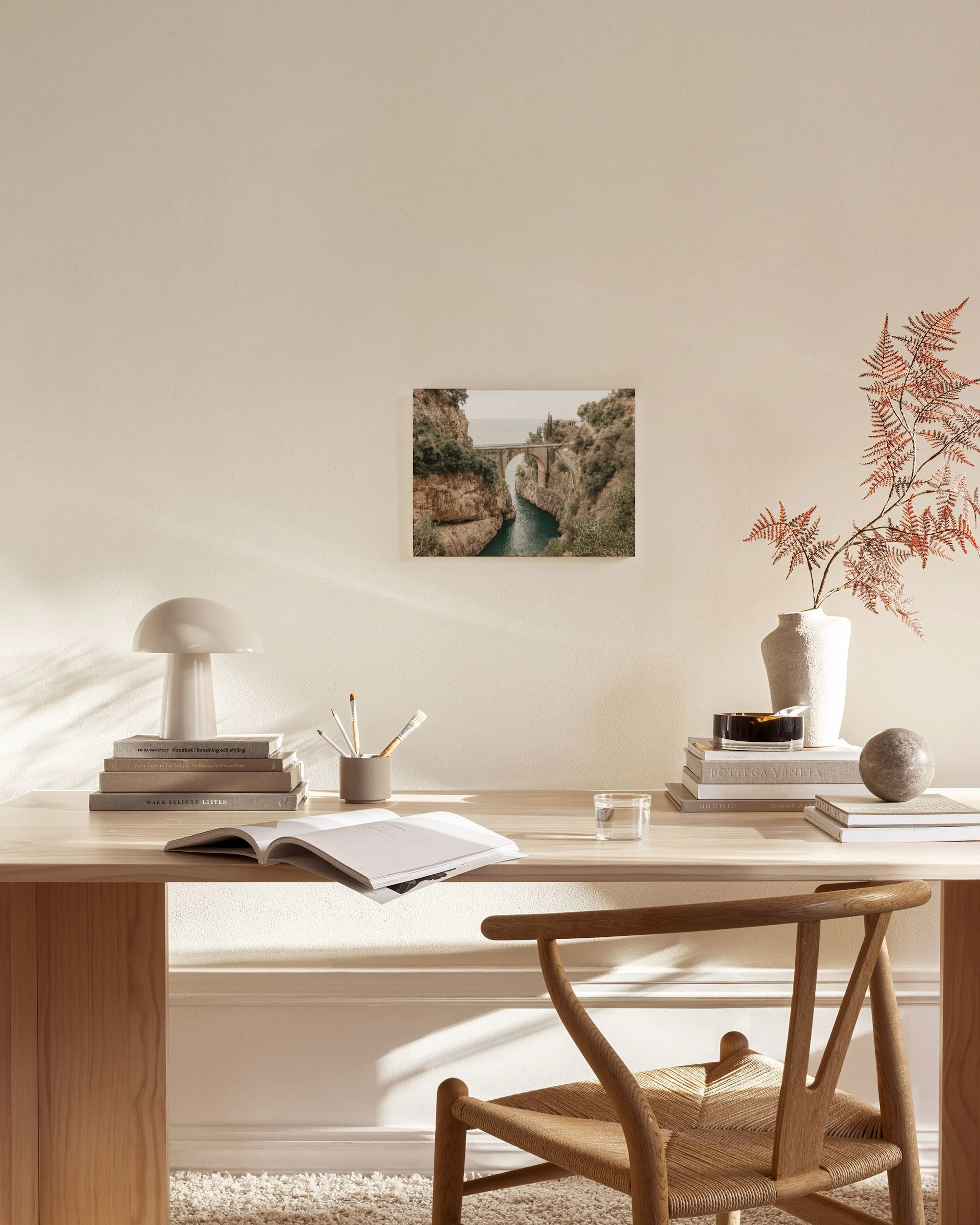 A canvas print of a natural stone bridge over a blue-green river in a rocky gorge, hanging above a console table in a minimalist