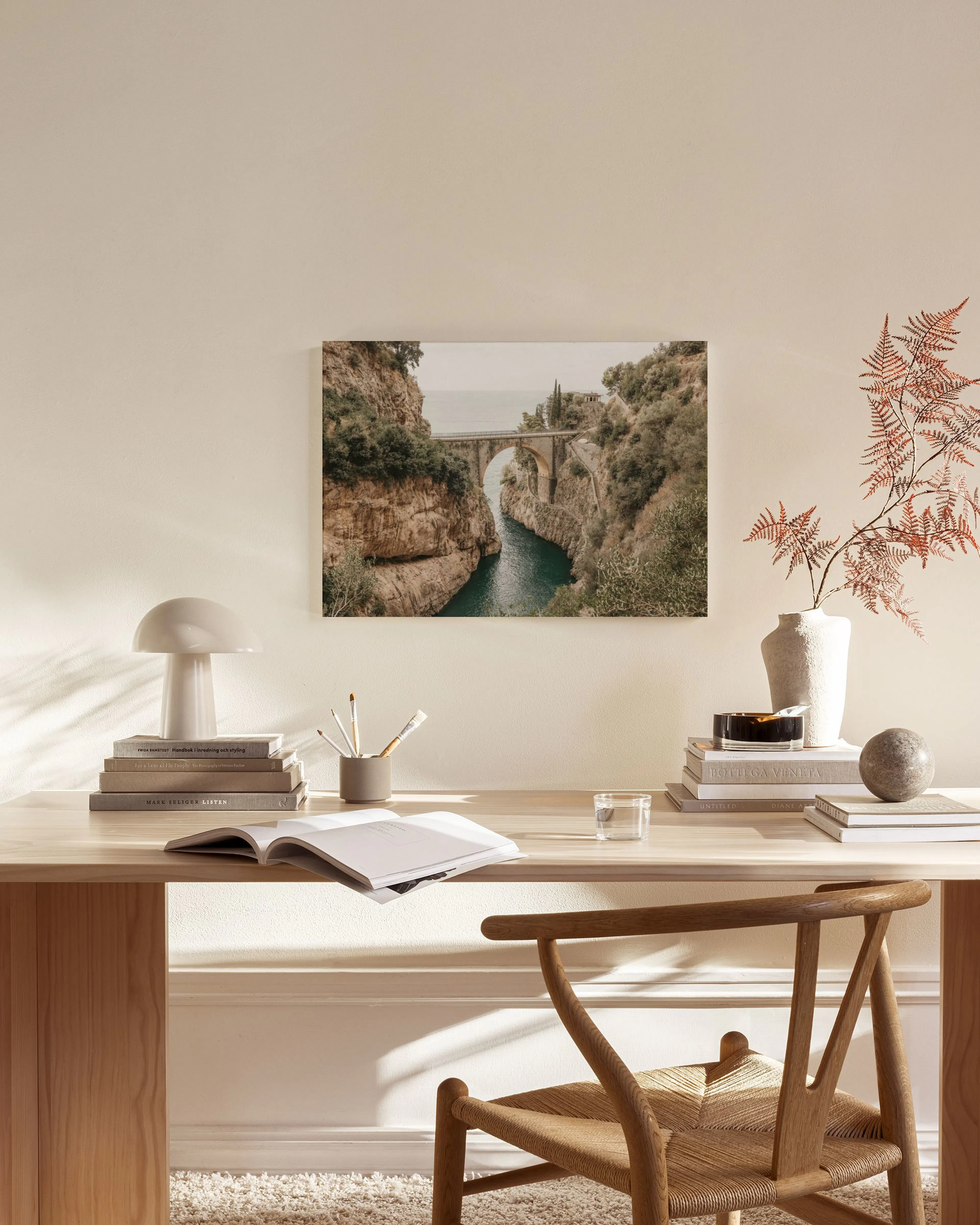 Lienzo con un puente de piedra sobre un río entre acantilados verdes, colgado en una sala de estar moderna sobre un mueble bajo.