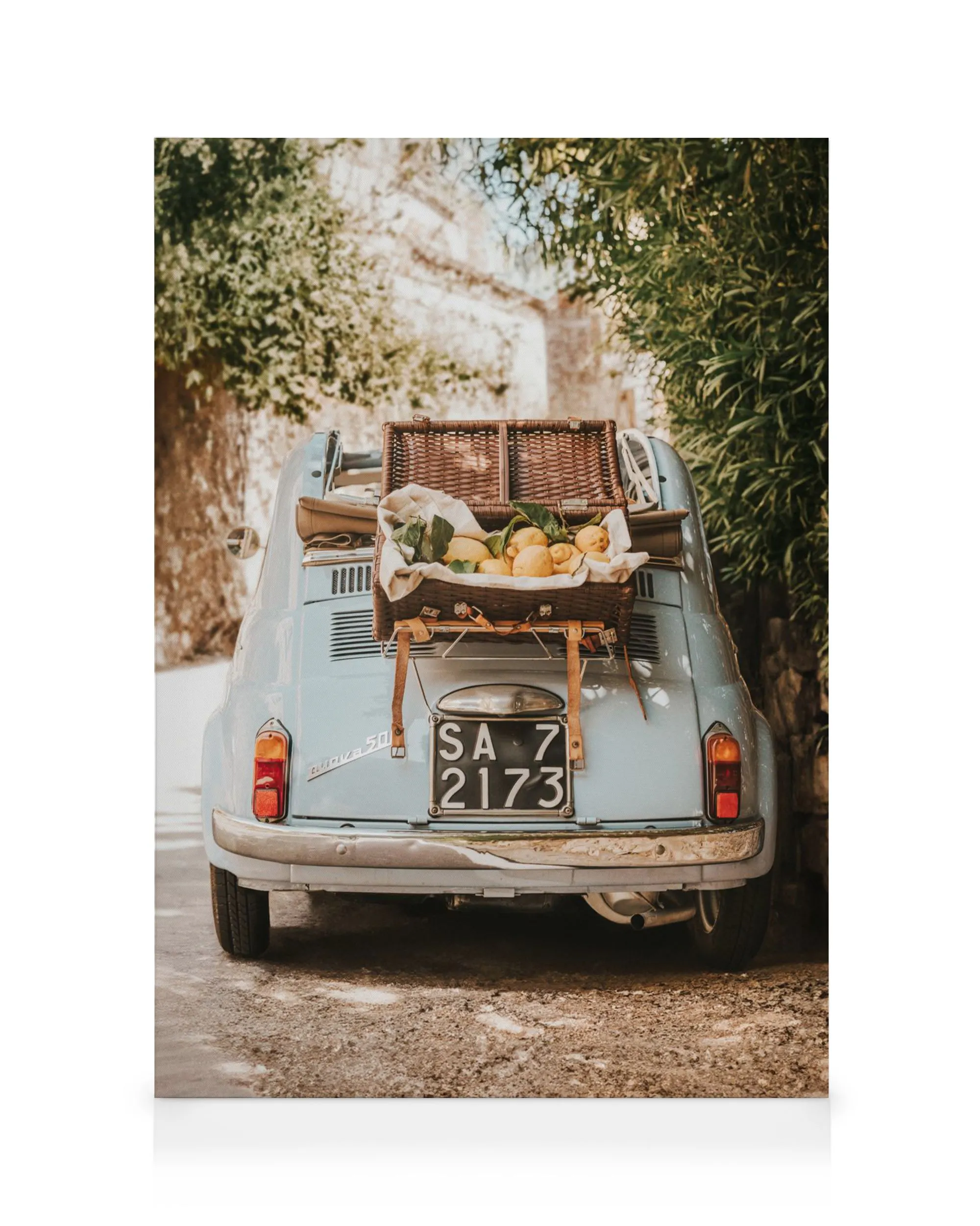 Coche vintage azul claro con cesta de picnic llena de limones amarillos y hojas verdes, fondo de pared y plantas.