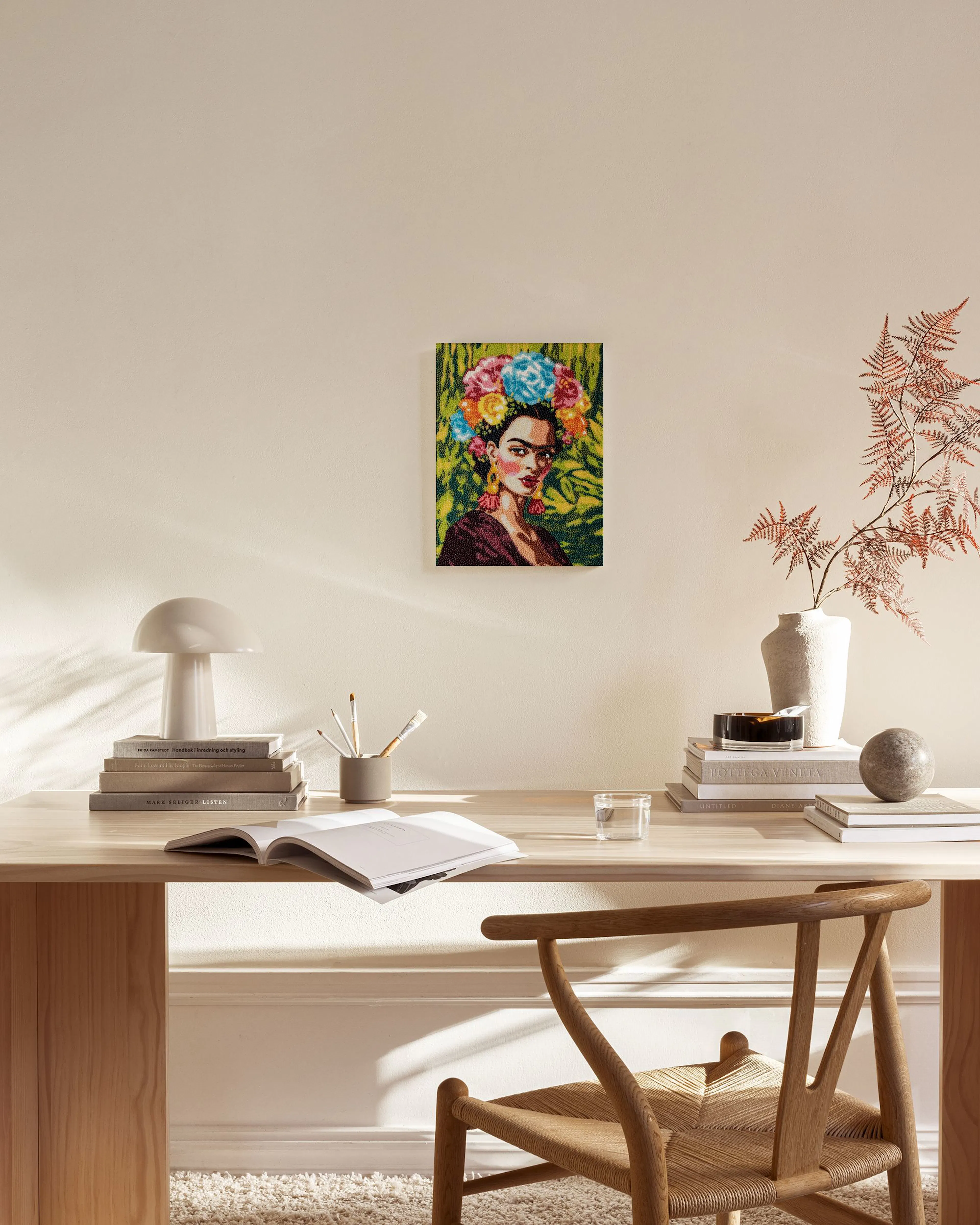 A colorful pointillism portrait of Frida Kahlo with a floral crown, hanging above a wooden console in a modern living room.