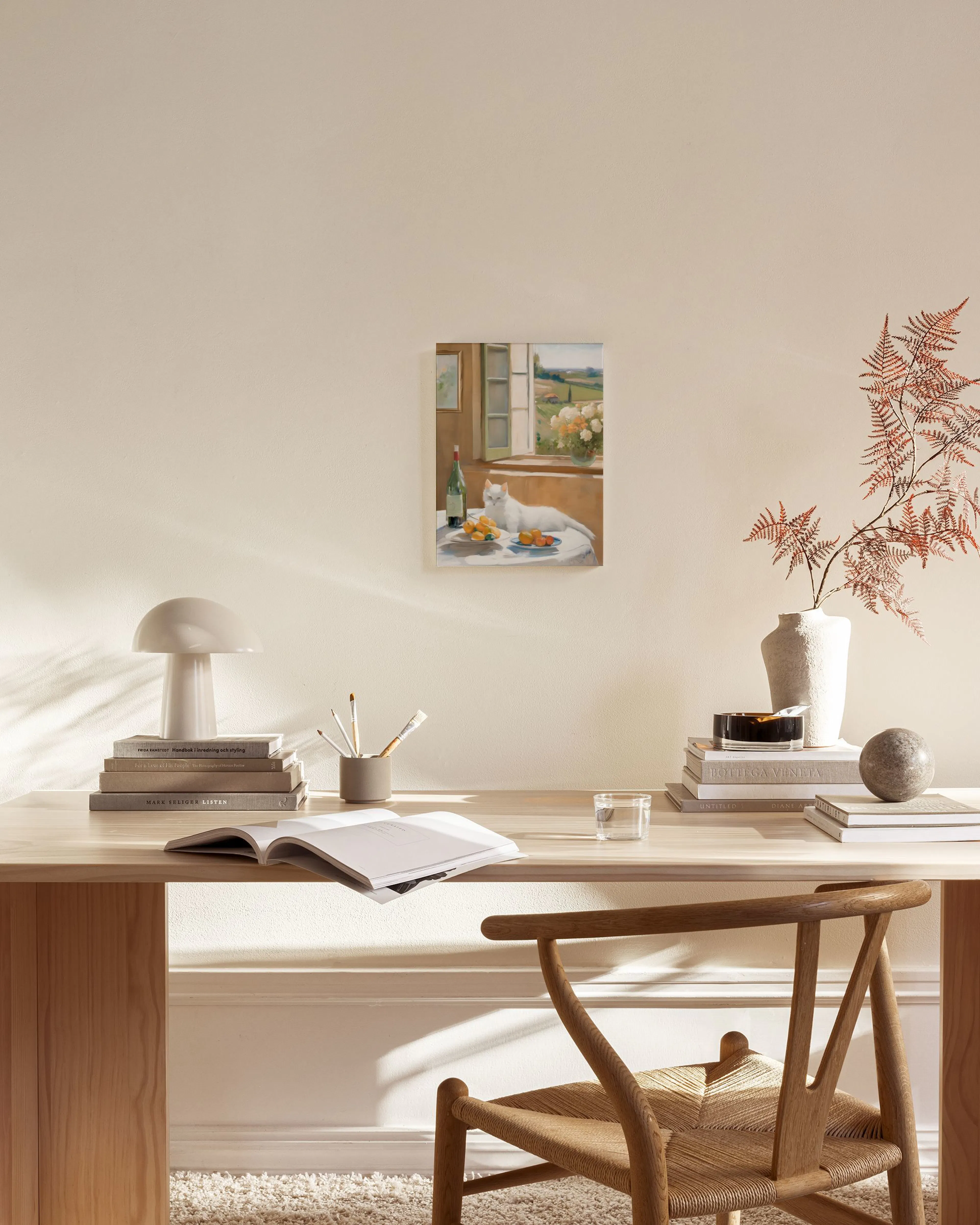 A canvas print of a white cat and fruit on a table by an open window, with a scenic view, hanging in a bright living room.