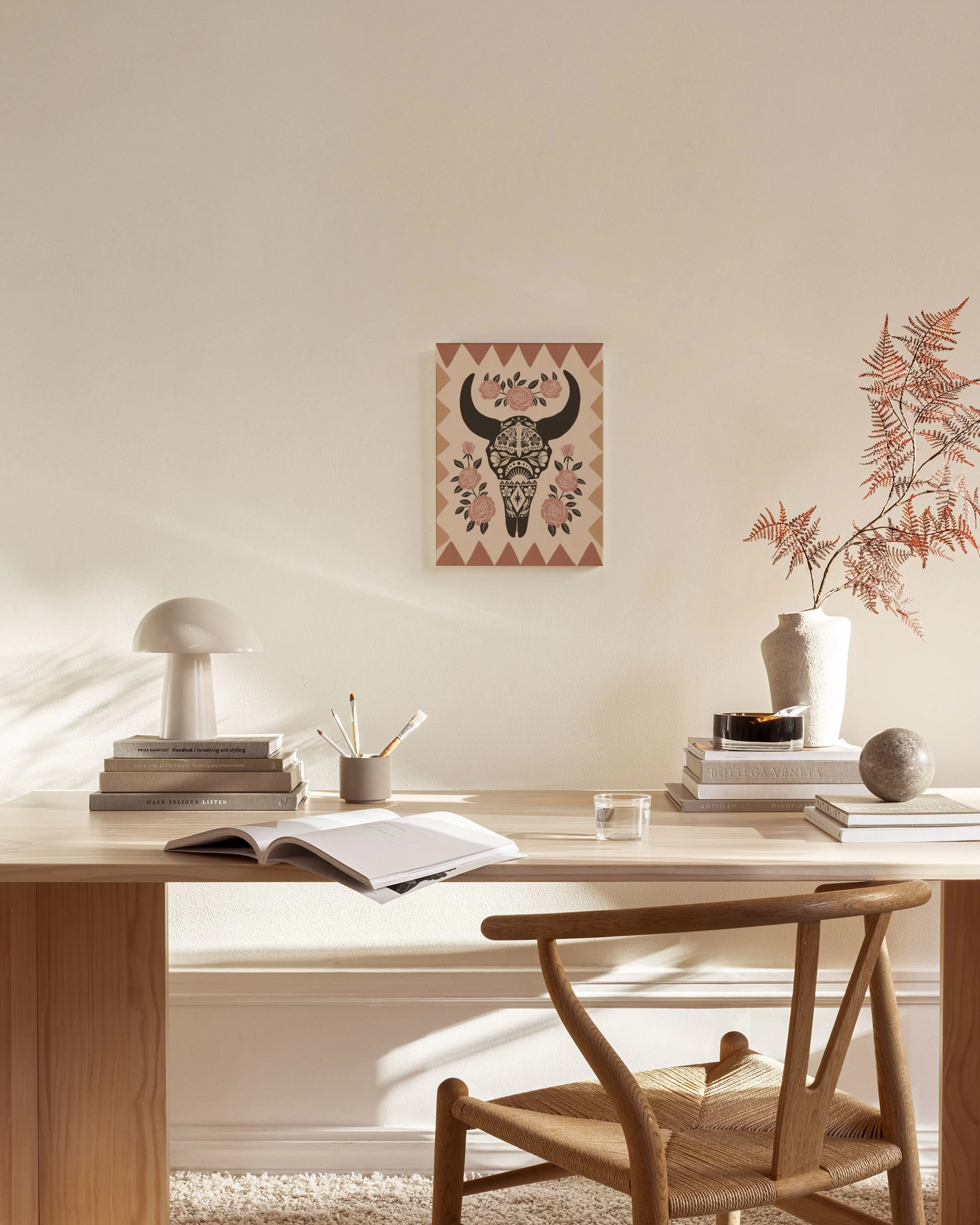 Lerretsbilde med oksehode og rosa roser, henger over en benk i en moderne stue med minimalistisk innredning.
