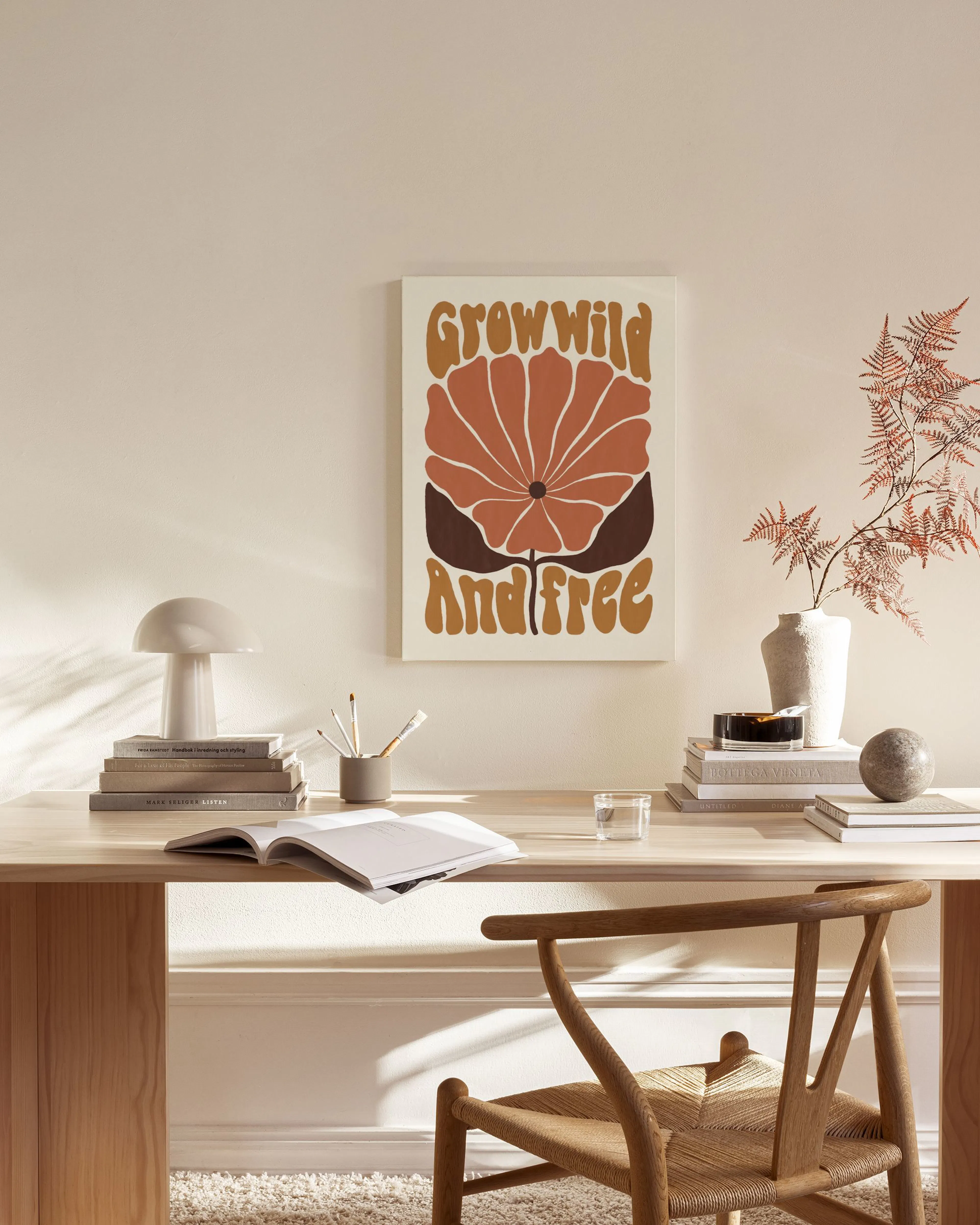 Tela decorativa com imagem de flor castanha e laranja com texto Grow Wild And Free, pendurada numa sala de estar com poltrona de