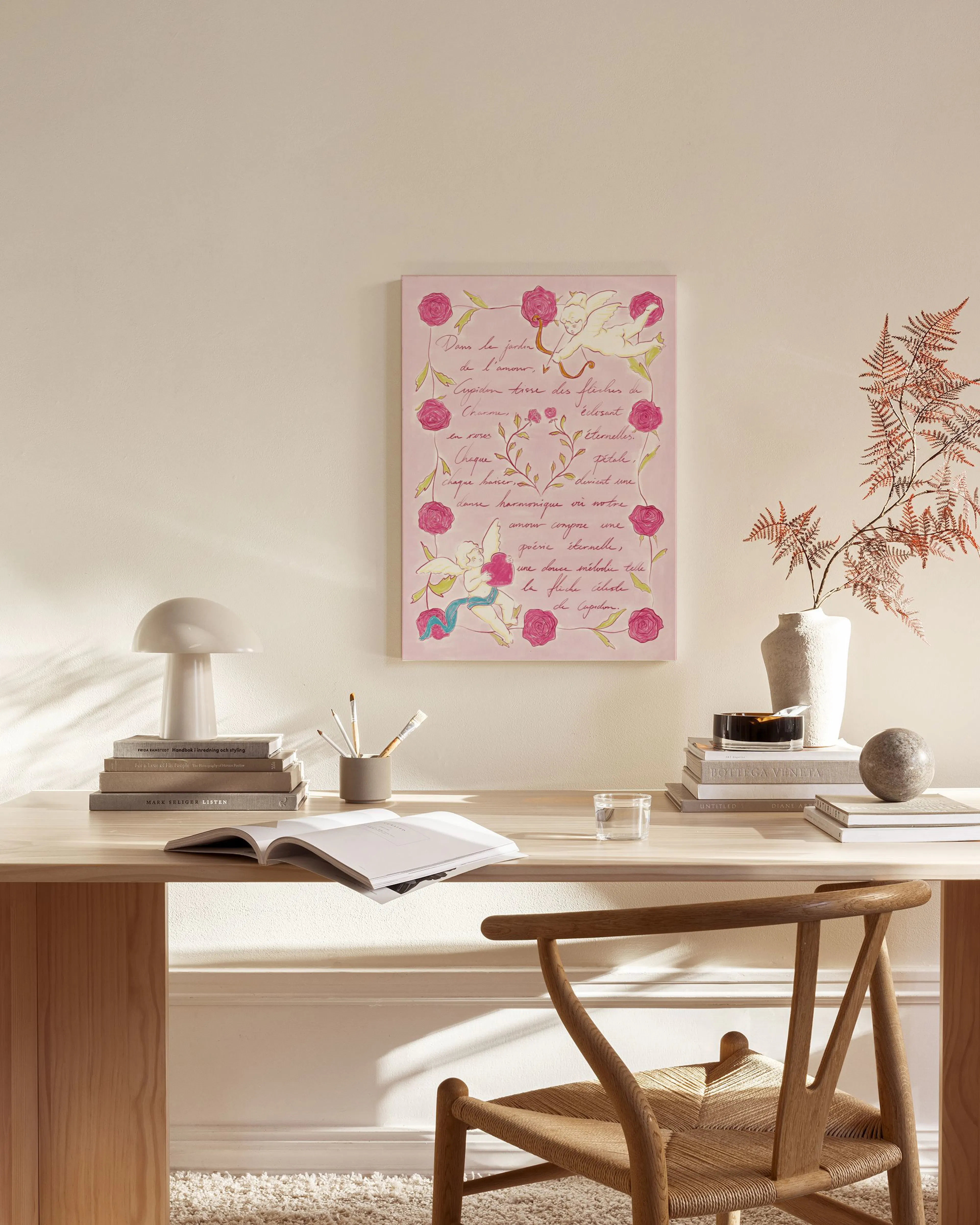 Leinwandbild mit rosa Hintergrund, roten Rosen, Engeln und französischer Schrift, hängt in einem modernen Wohnzimmer über einem 