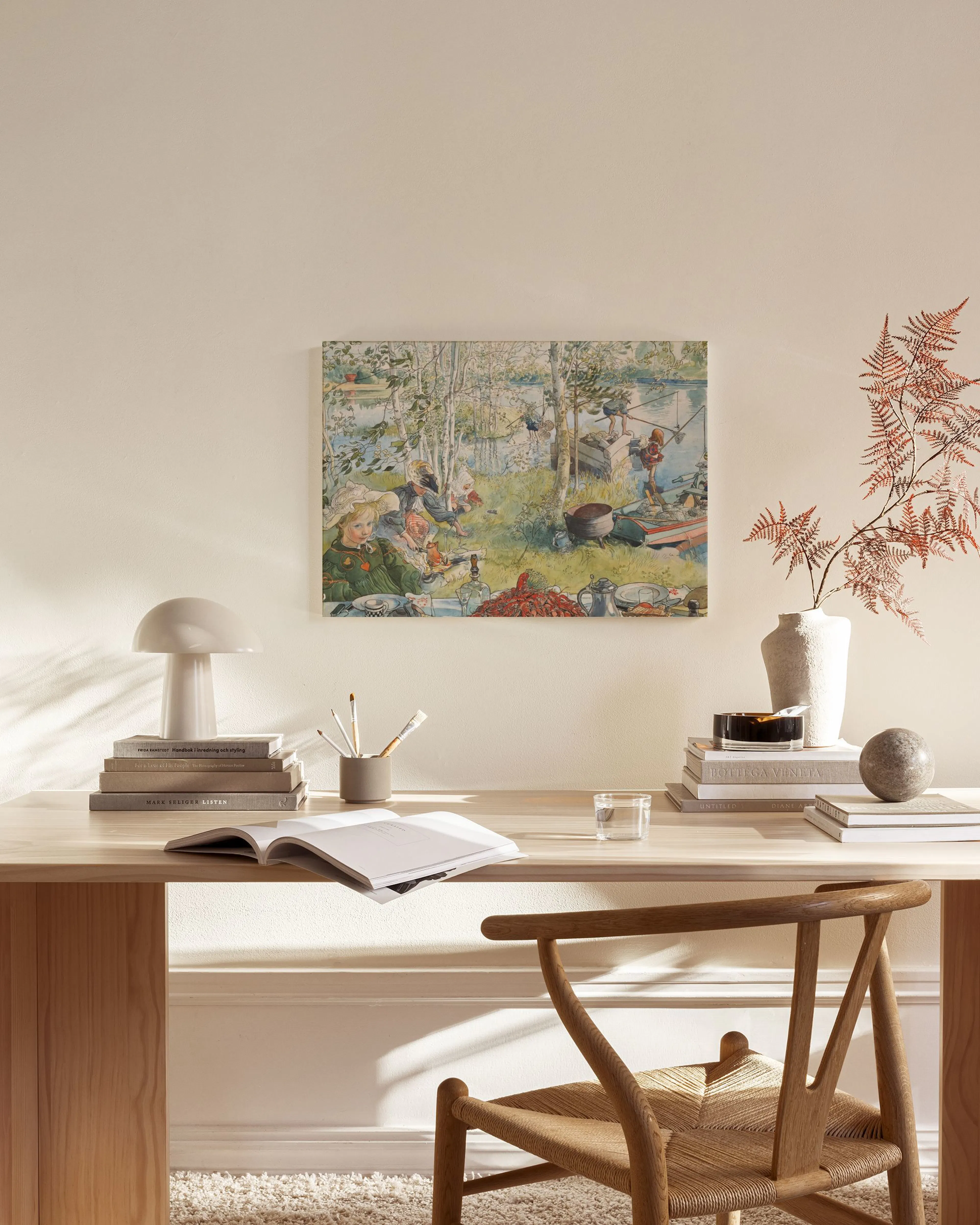 A canvas print of people picnicking by a lake with trees, in a modern living room above a wooden console table.