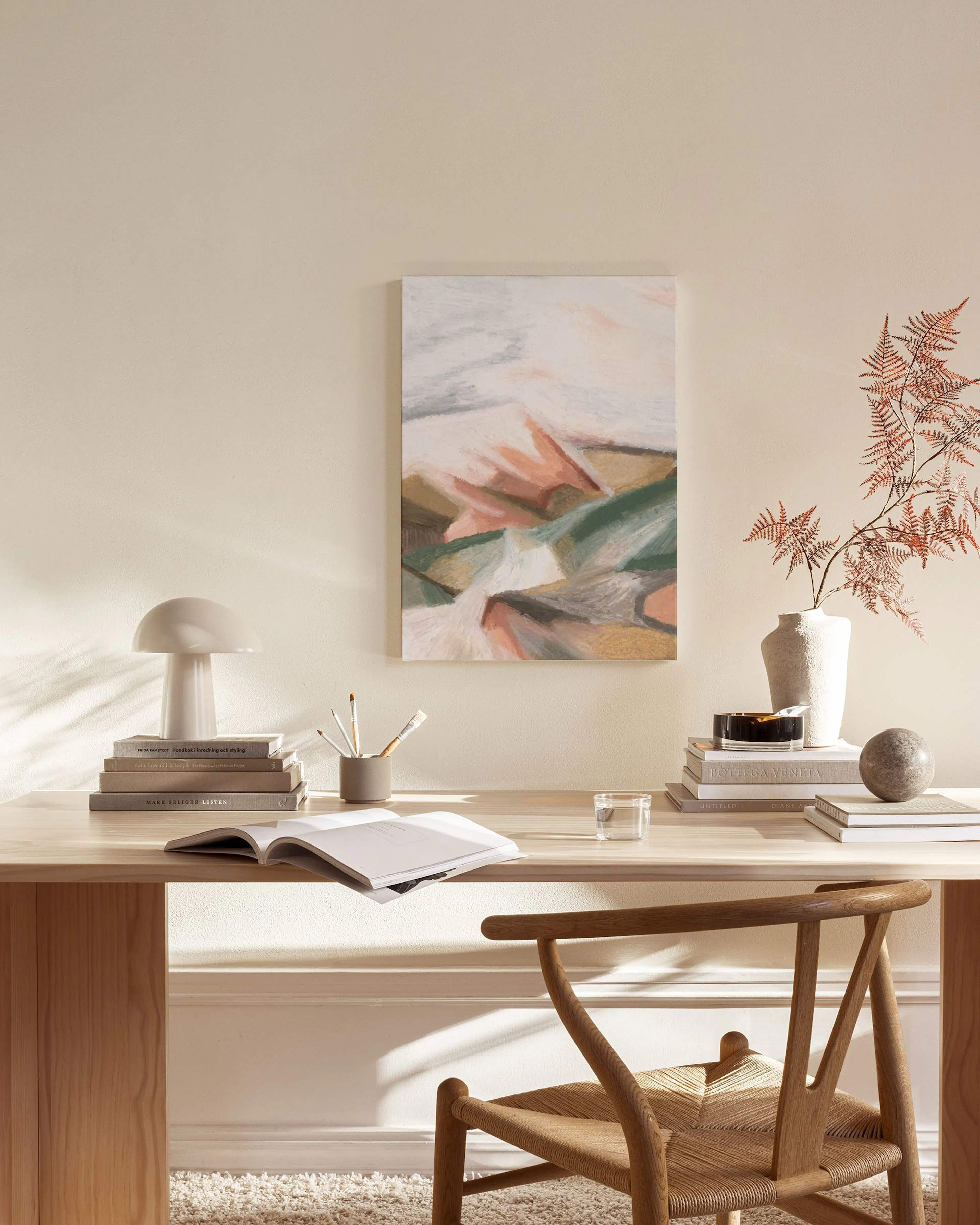 Abstract canvas print with geometric shapes in muted green, pink, and beige, hanging in a minimalist living room.