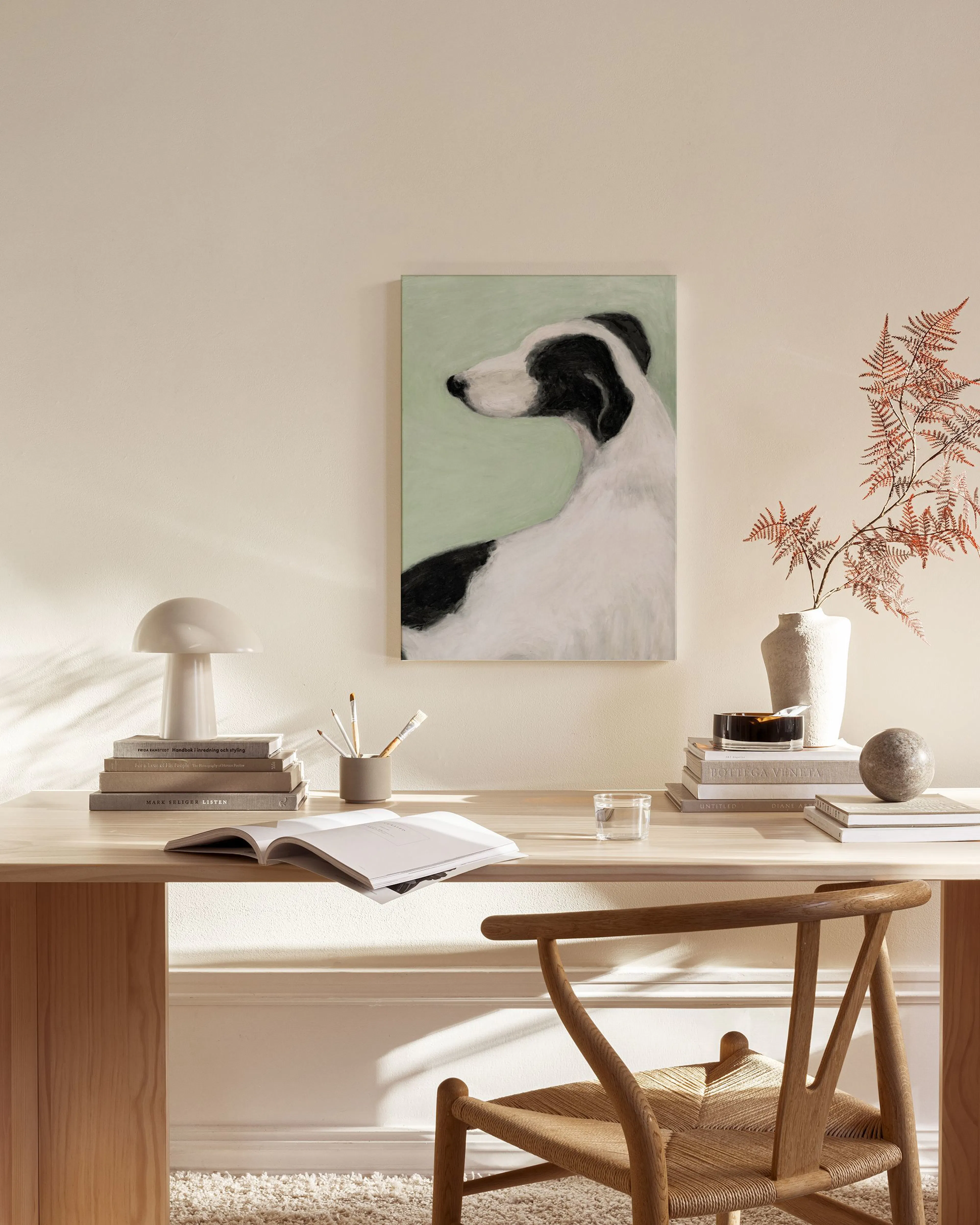 A canvas print of a black and white dog on a light green background, hanging above a wooden console table in a minimalist living
