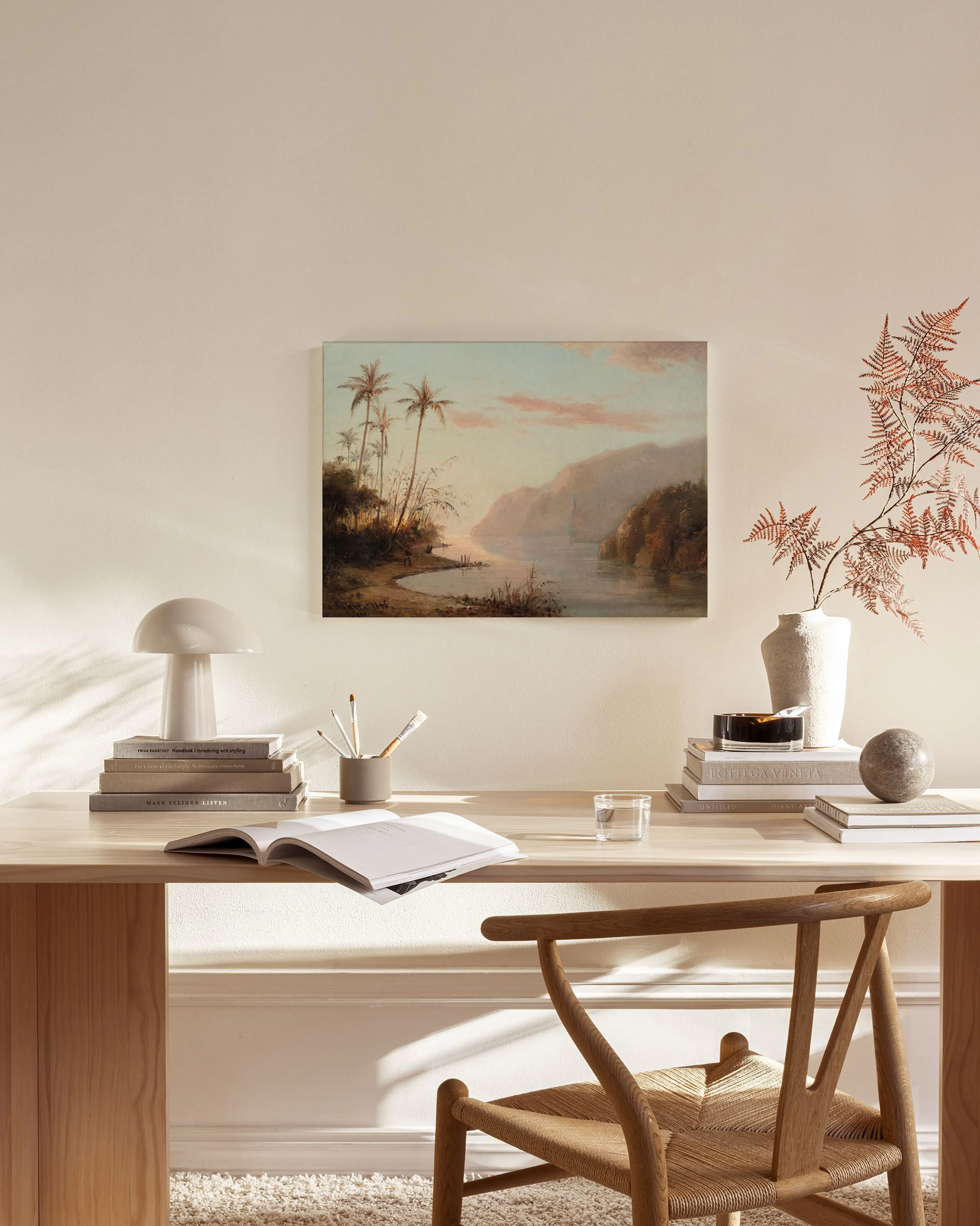 A tropical landscape painting with palm trees by a river and mountains under a pink sky, hanging above a wooden console table in