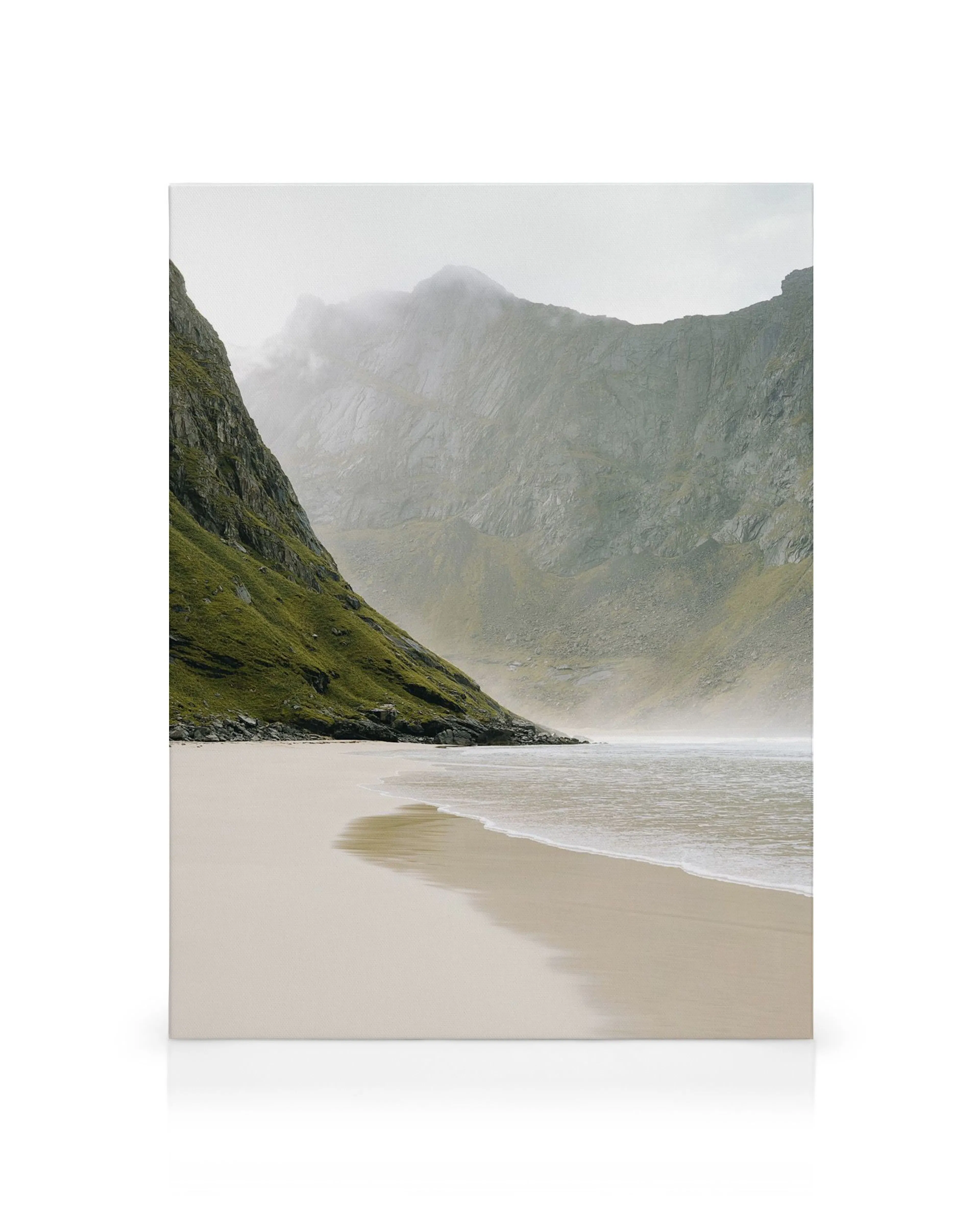 Silent Bay canvas print: A serene beach with light sand and gentle waves, flanked by a steep, mossy green mountain and distant m