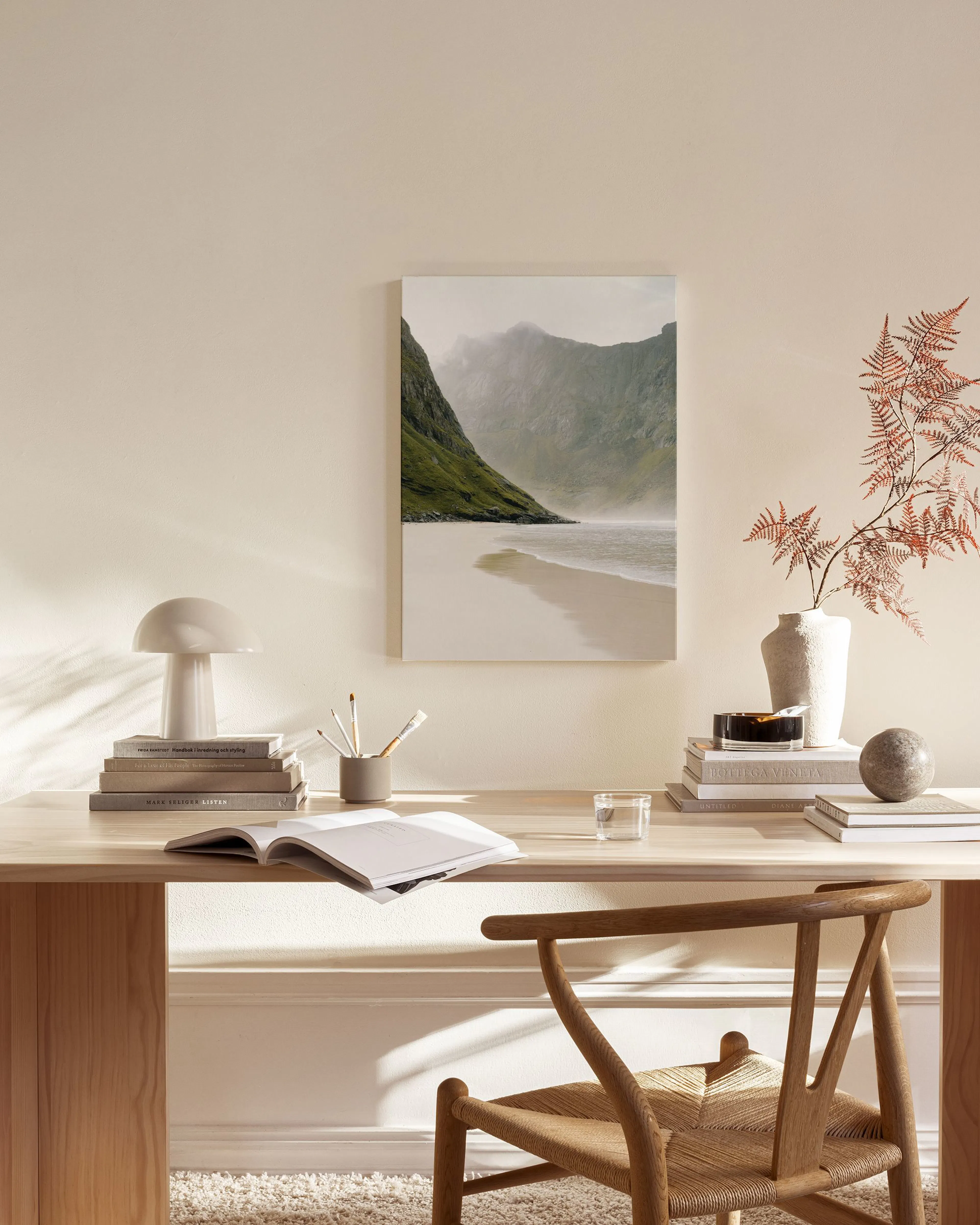 A canvas print of a misty green mountain next to a sandy beach and crashing waves, displayed in a neutral-toned living room.