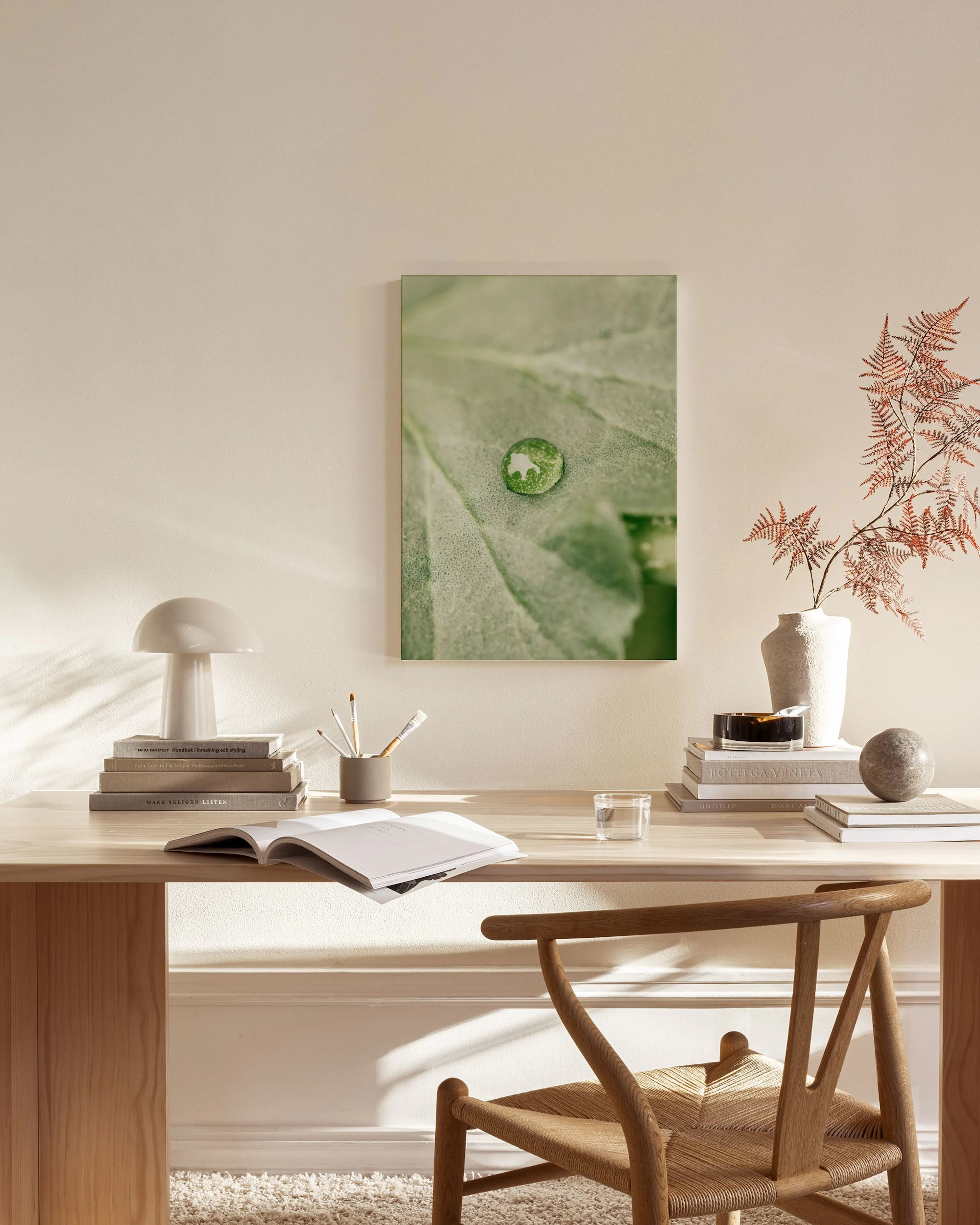 A canvas print of a green leaf with a water droplet, on a light wall in a minimalist living room.