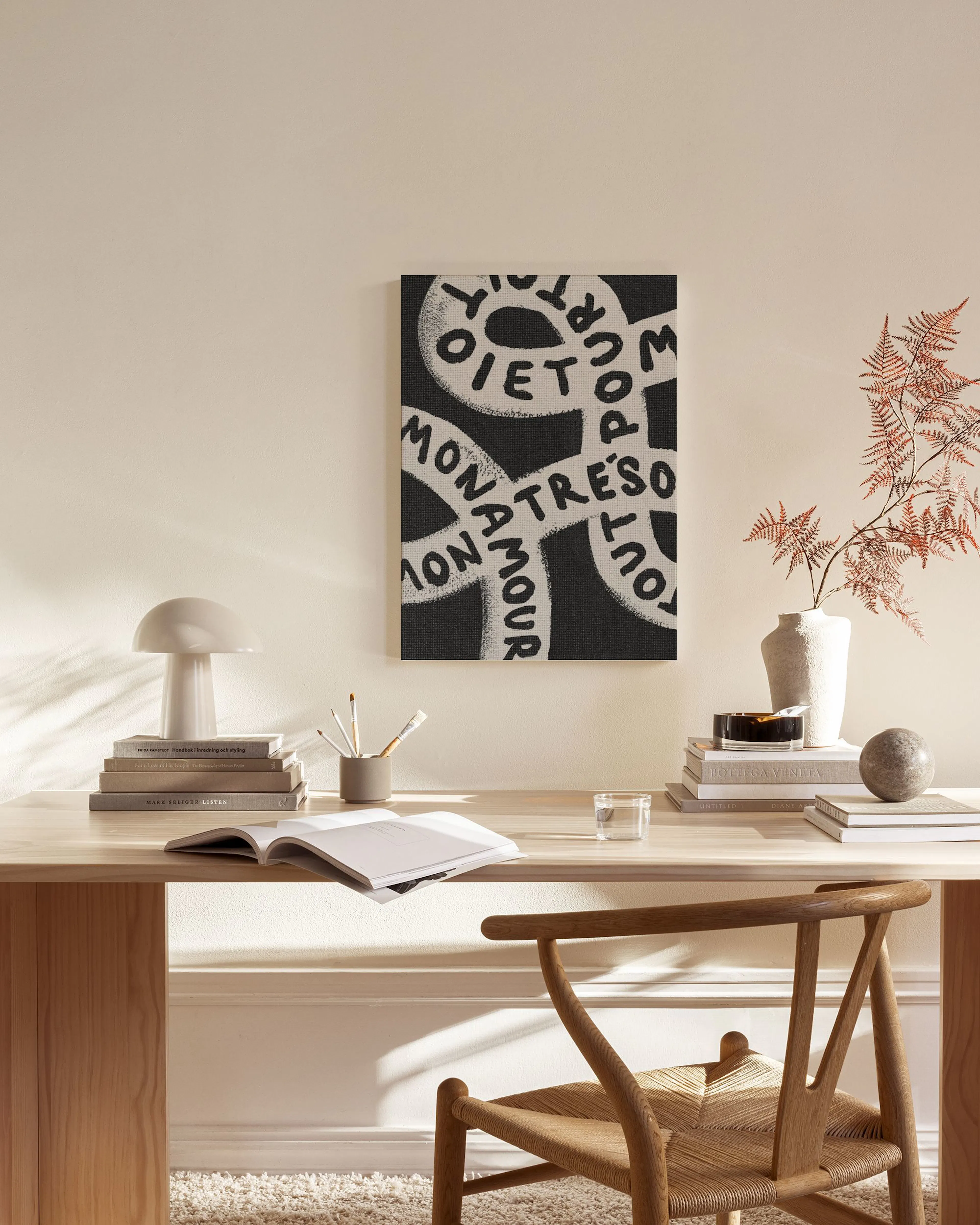 Canvastavla med svart bakgrund och vita, slingrande ord som MON AMOUR, hängande i ett ljust vardagsrum med trädetaljer.