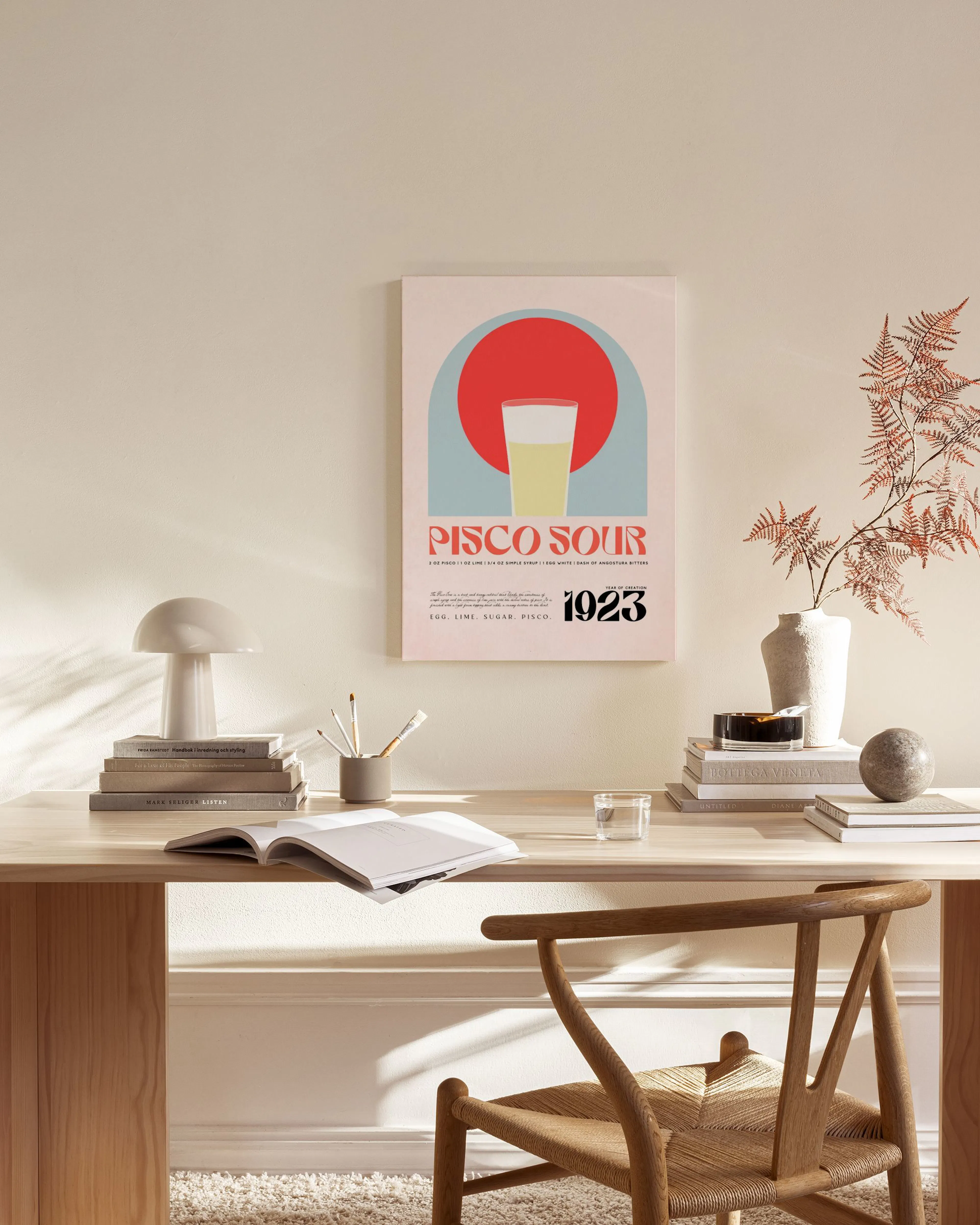 A Pisco Sour poster with a red circle and light blue arch, hanging in a minimalist living room above a wooden console.