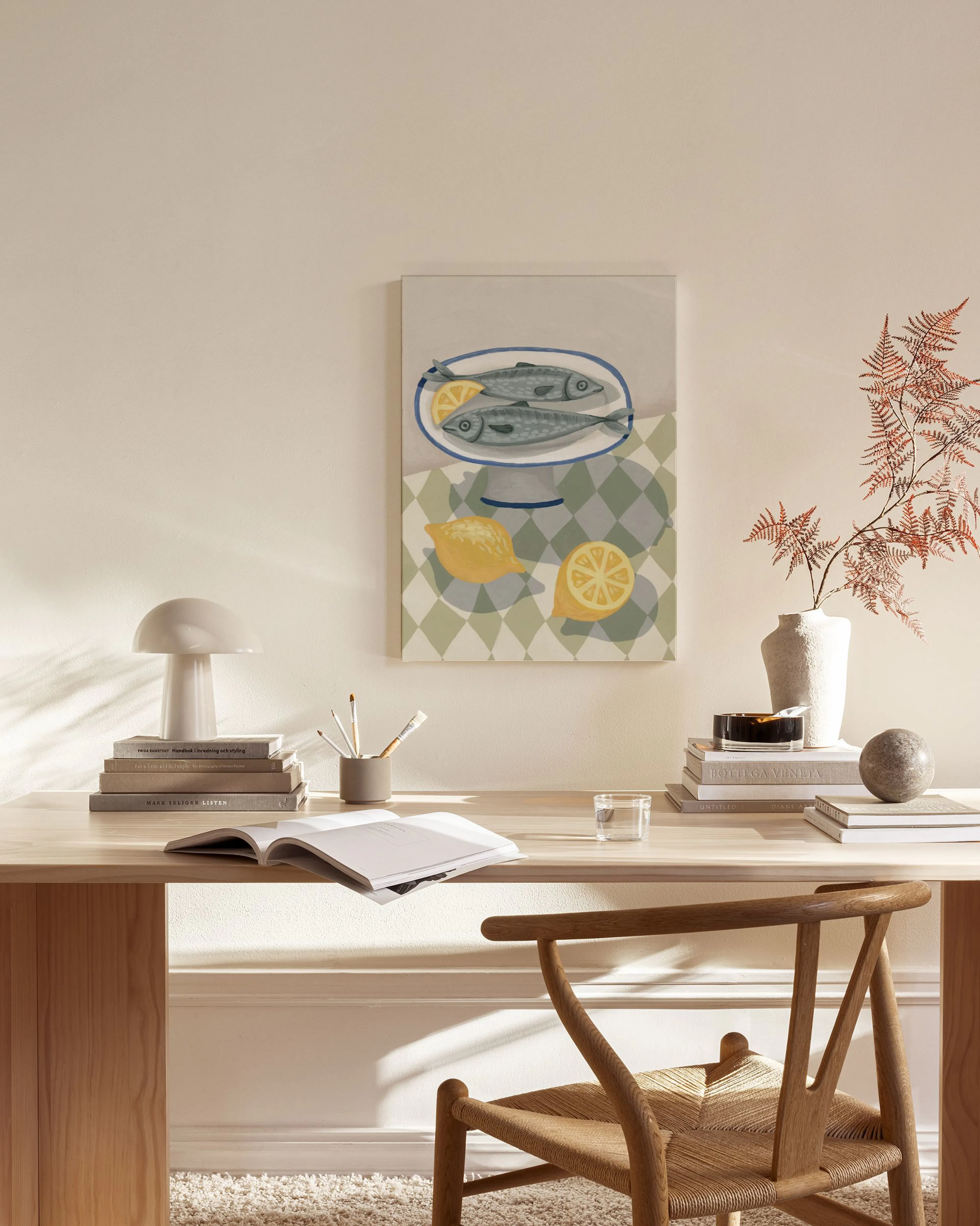 Een canvas met twee vissen en citroenen op een geruit tafelkleed, hangend in een lichte woonkamer boven een houten dressoir.