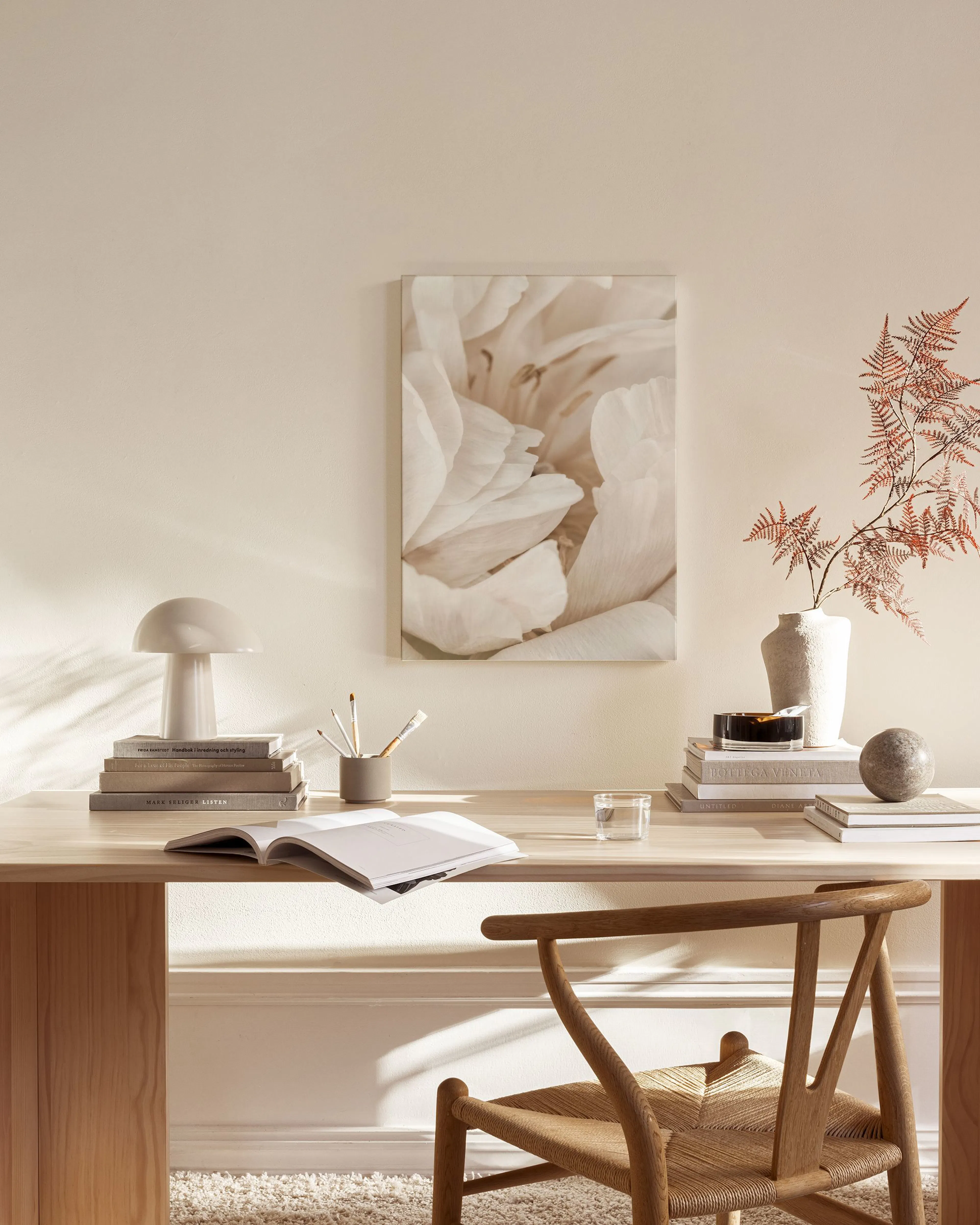 A canvas print of white and beige flower petals hanging in a minimalist living room above a wooden console.