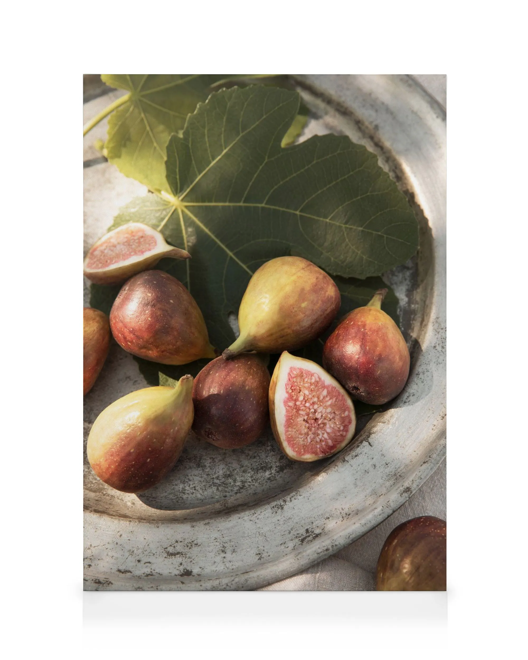 Sun-ripened fresh figs and green fig leaves on a rustic plate, one fig sliced open revealing its red pulp.