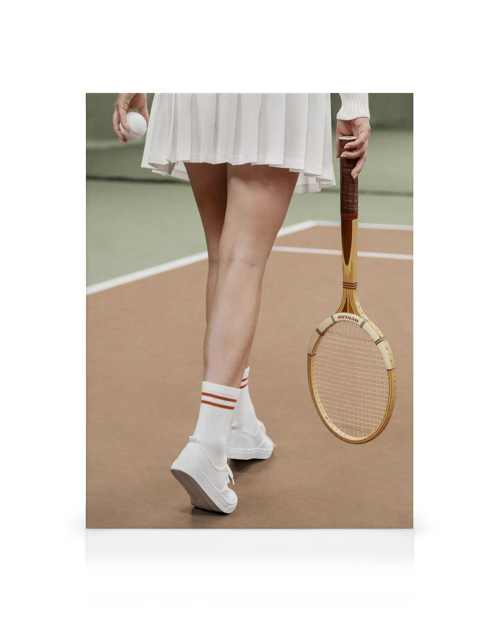 Fotografía de una tenista con falda blanca, calcetines a rayas, zapatillas y raqueta sobre cancha de arcilla.
