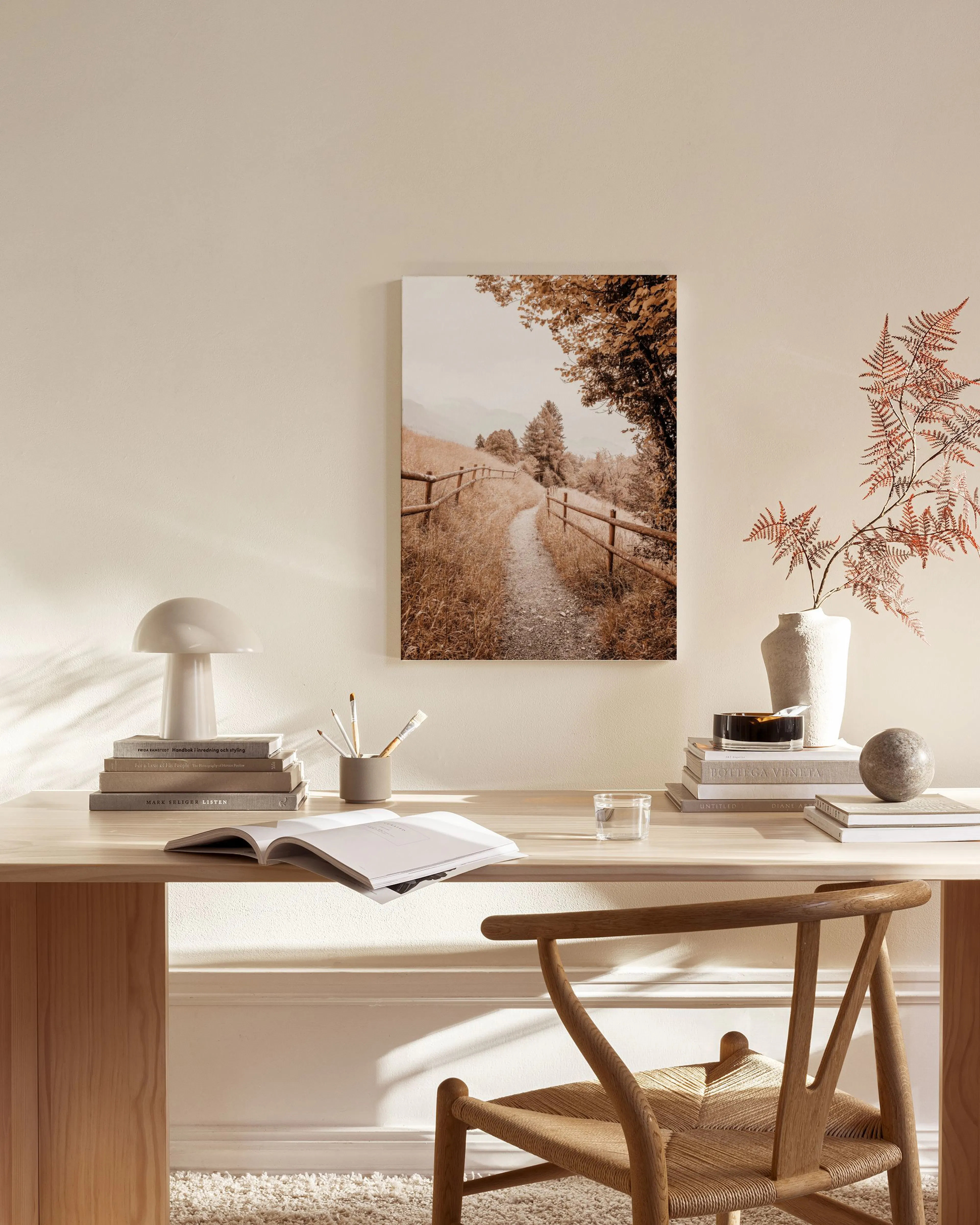 A canvas print of a mountain path with a wooden fence and autumn trees, hanging in a minimalist living room.