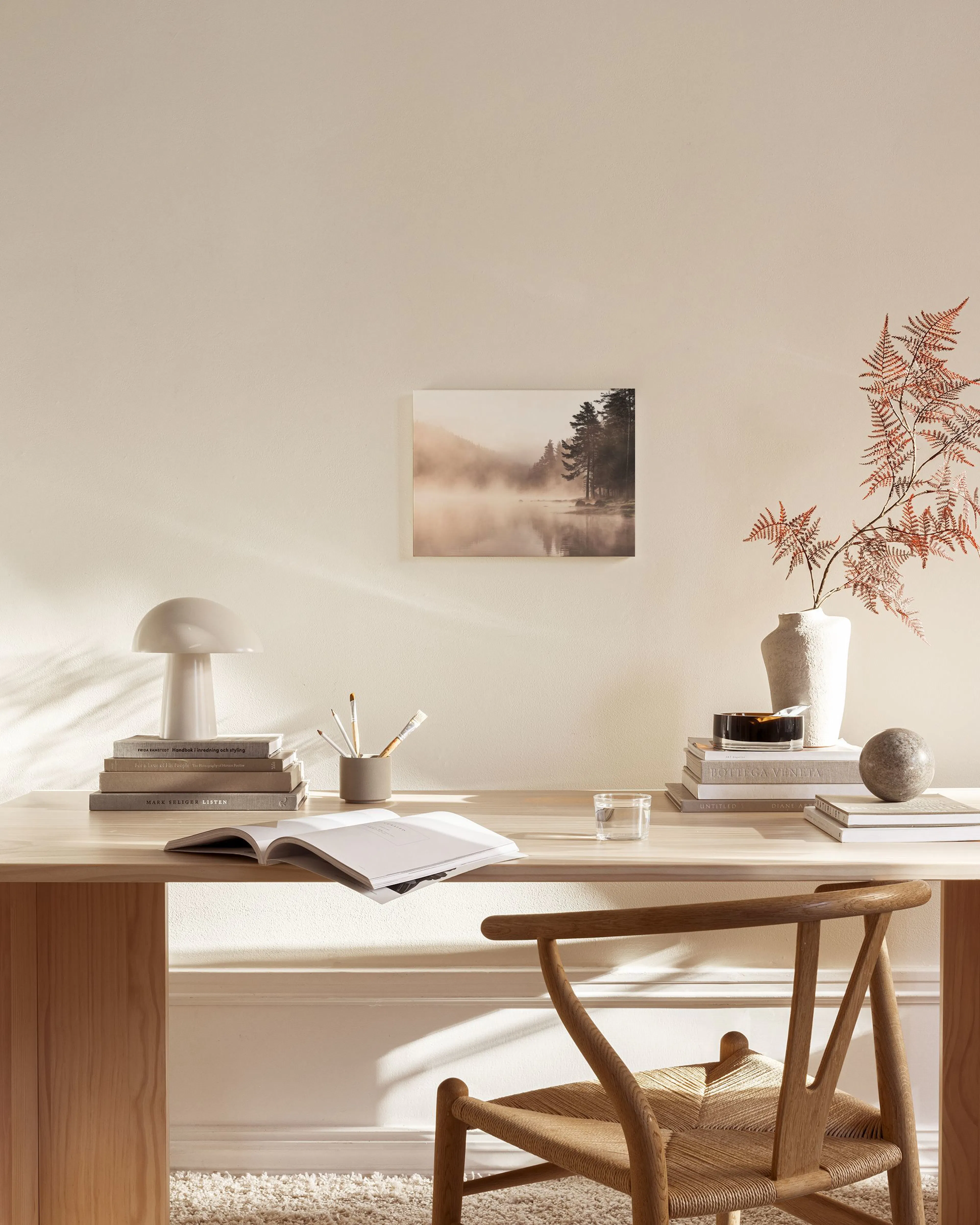Toile paysage brumeux avec un lac et des pins, accrochée au-dessus dun meuble bas dans un salon moderne.