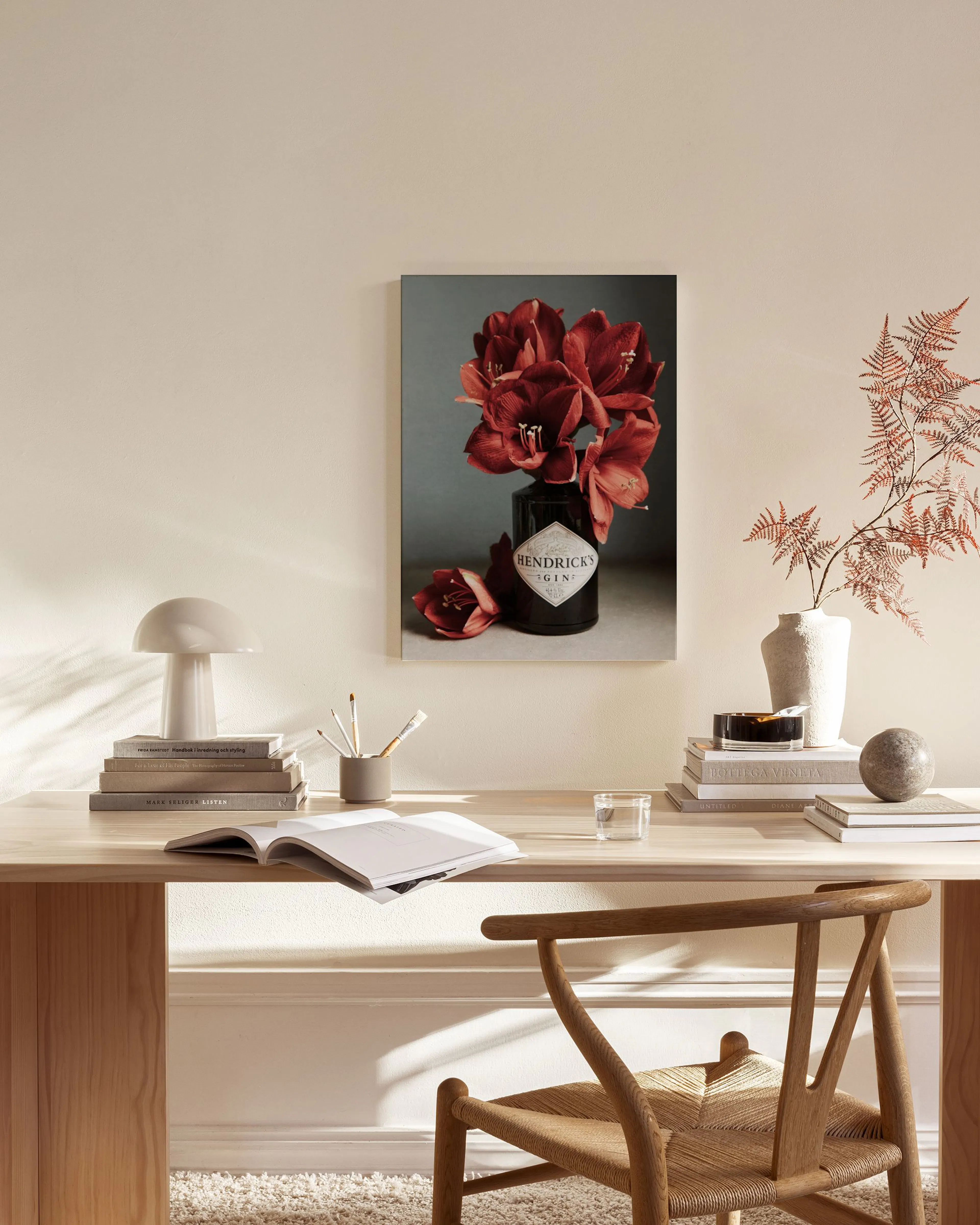 Canvastavla med röda amaryllis i en mörk flaska, hängande i ett ljust vardagsrum över en träbänk.