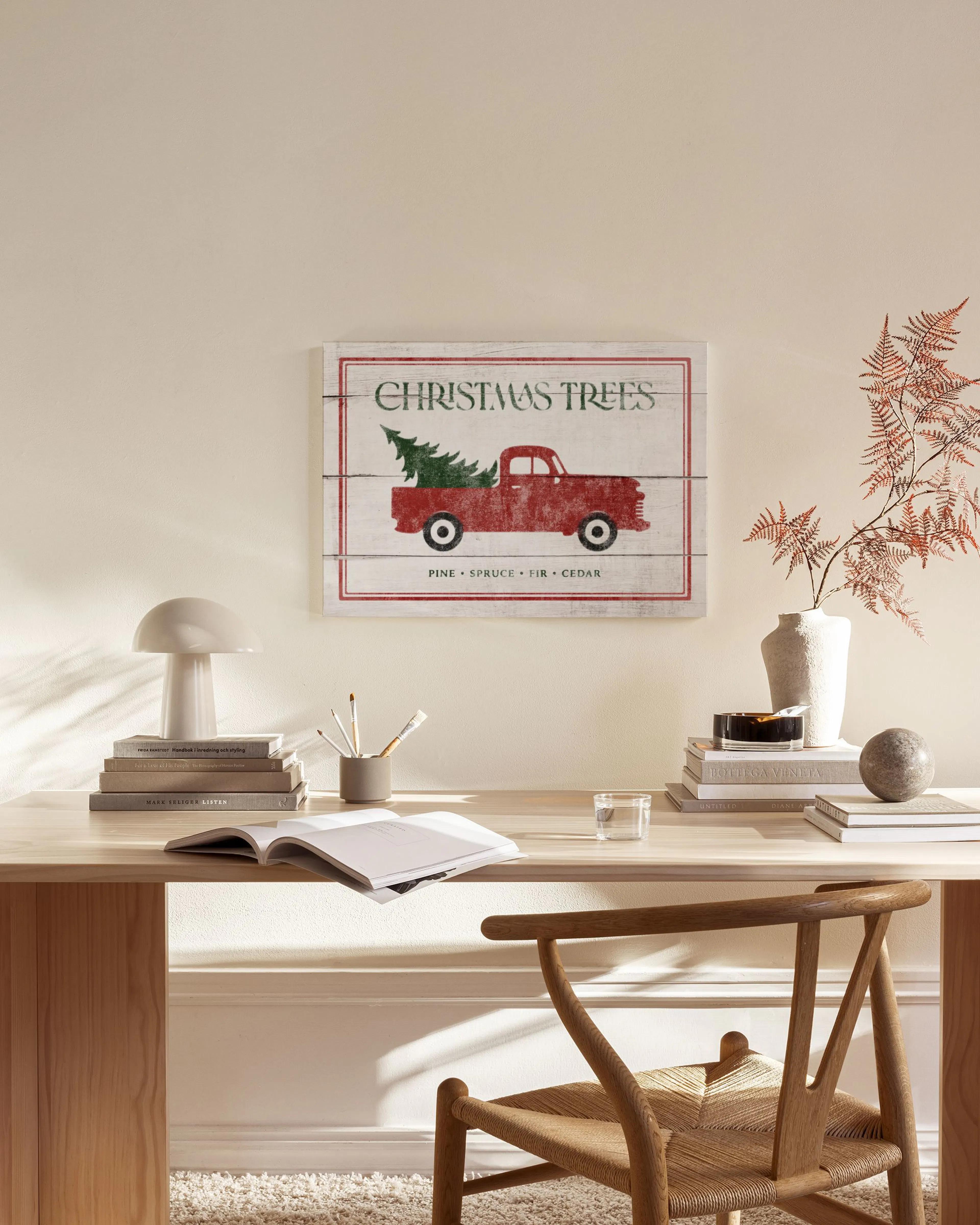 Lærred med billede af en julerød lastbil med et grantræ bagpå, hængende i en stue over en træbænk.