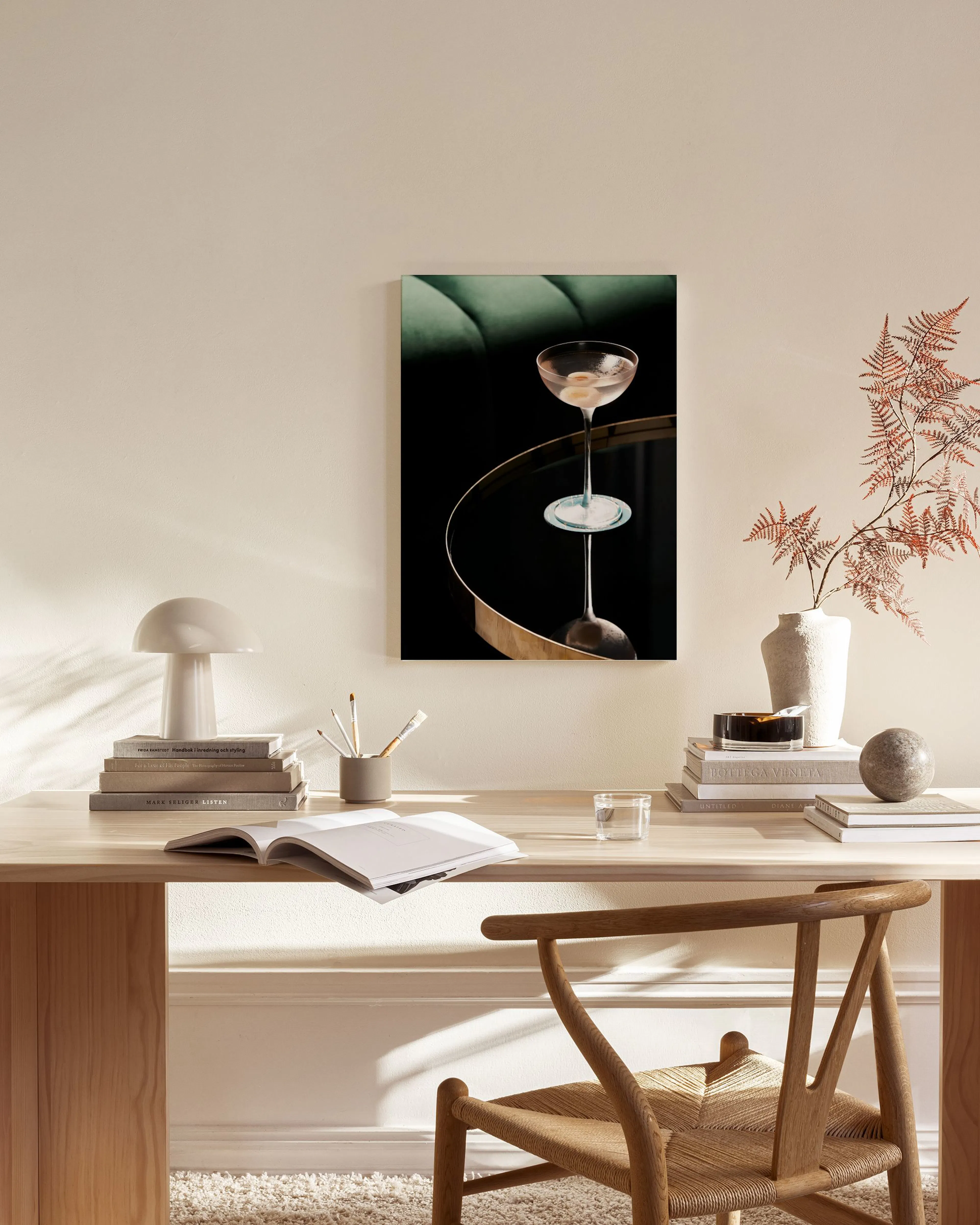 A cocktail glass with olives on a reflective surface, a dark green sofa in the background, hanging in a modern living room.