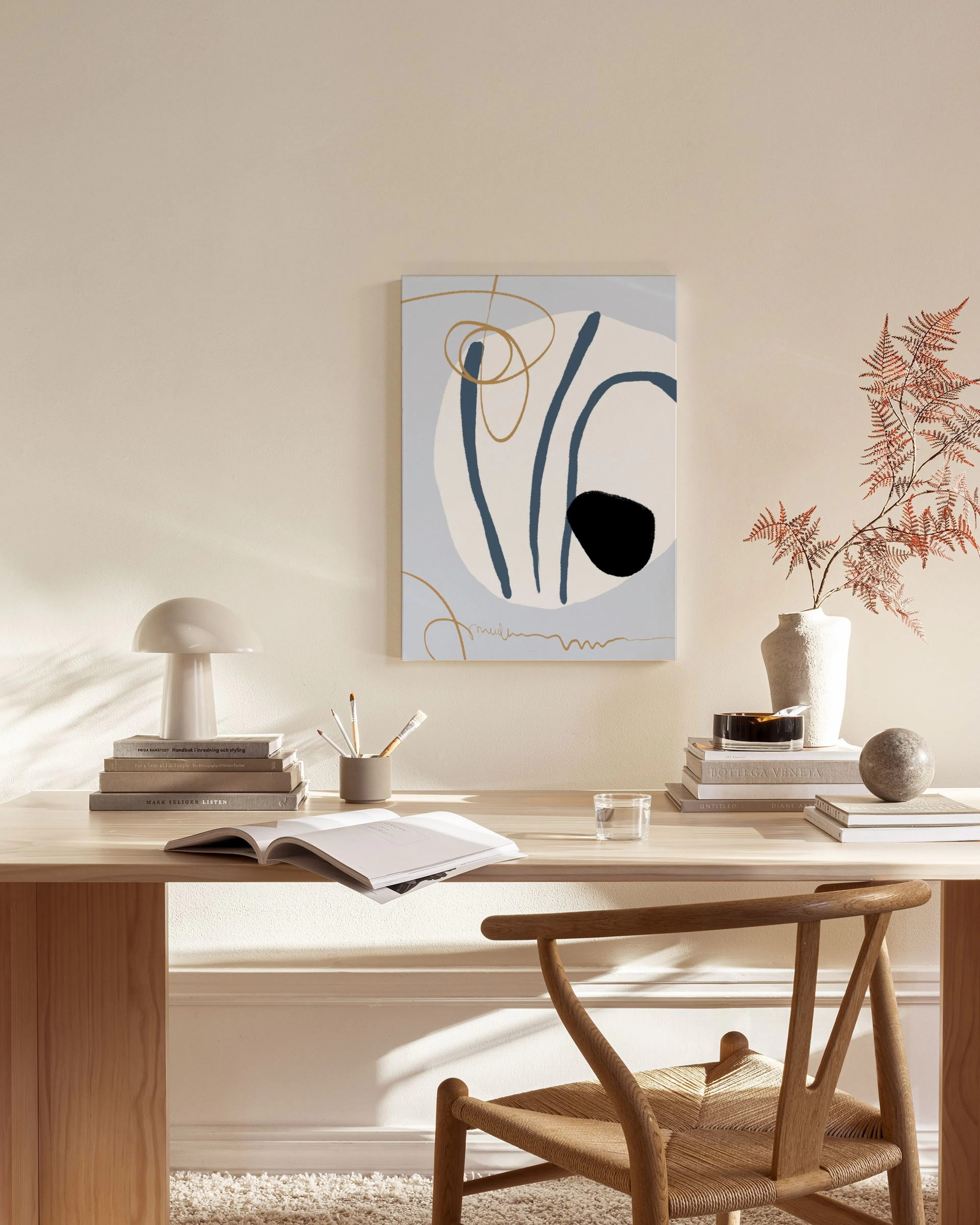 Lienzo abstracto con formas orgánicas en azul, blanco, negro y líneas doradas, colgado sobre un mueble bajo junto a un sillón de