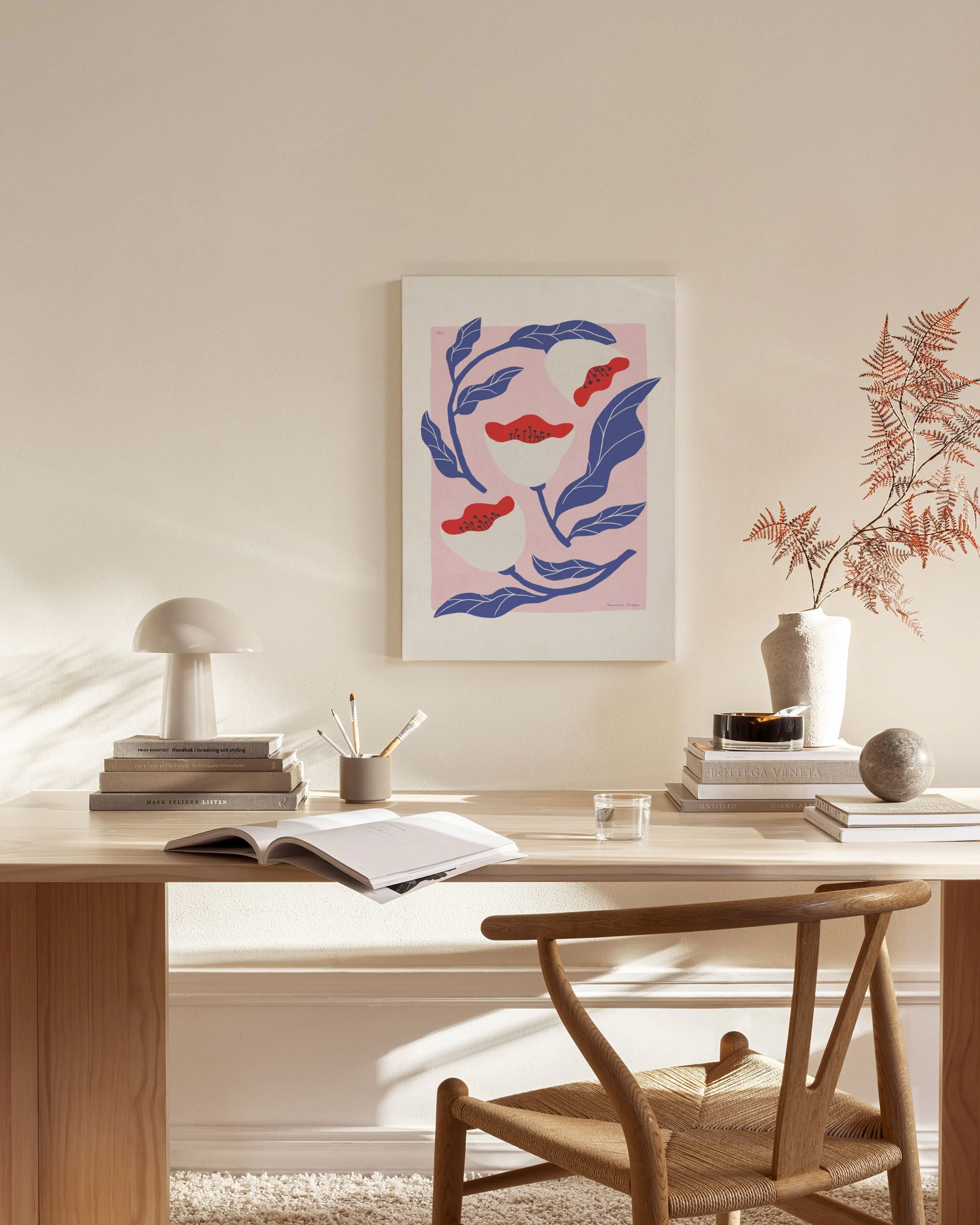 Canvas met roze achtergrond, blauwe bladeren en stervormige bloemen met rode accenten, hangend in een lichte woonkamer.
