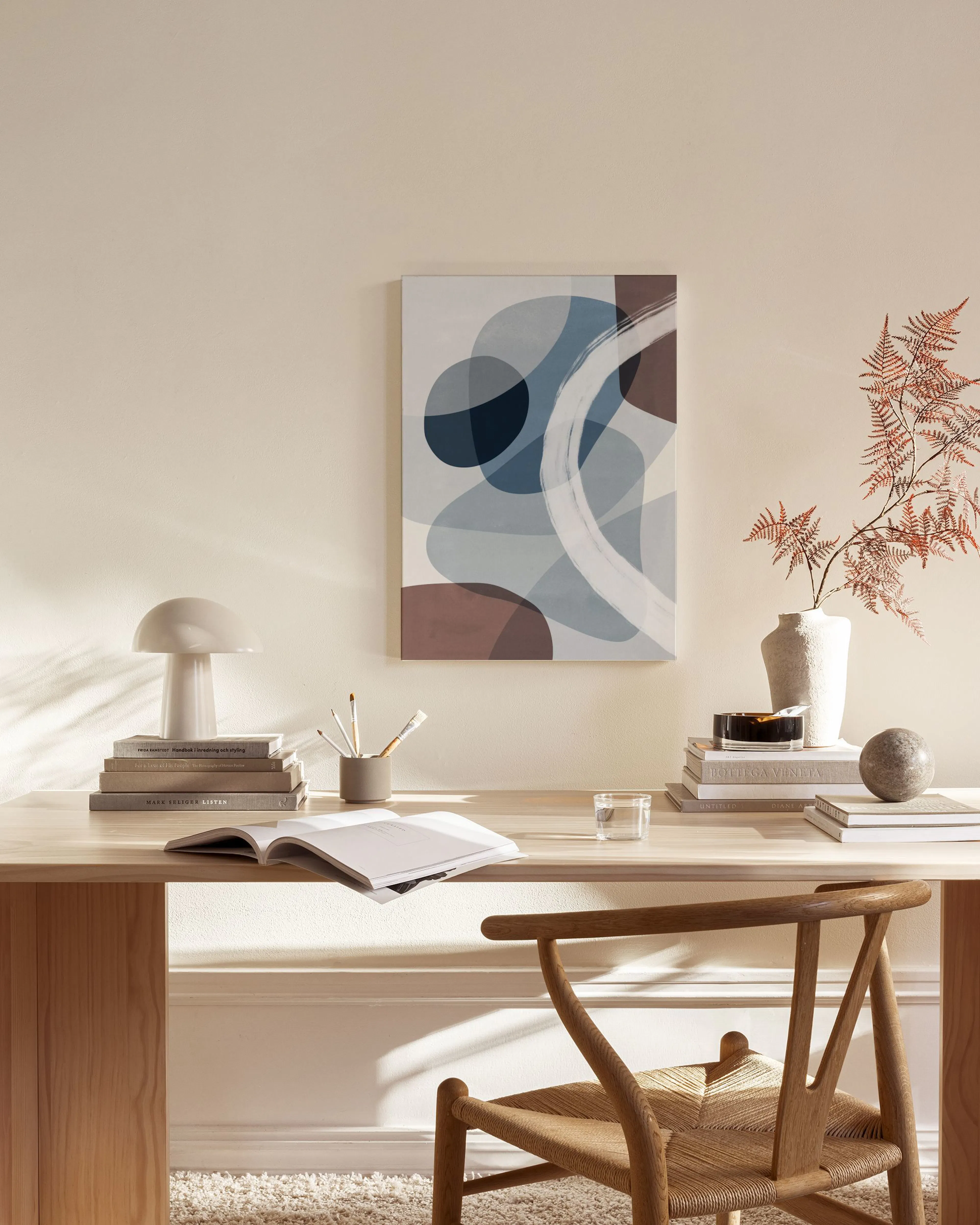 Tela decorativa abstrata com formas orgânicas azuis, castanhas e cinzentas sobrepostas, com pinceladas brancas, pendurada numa s