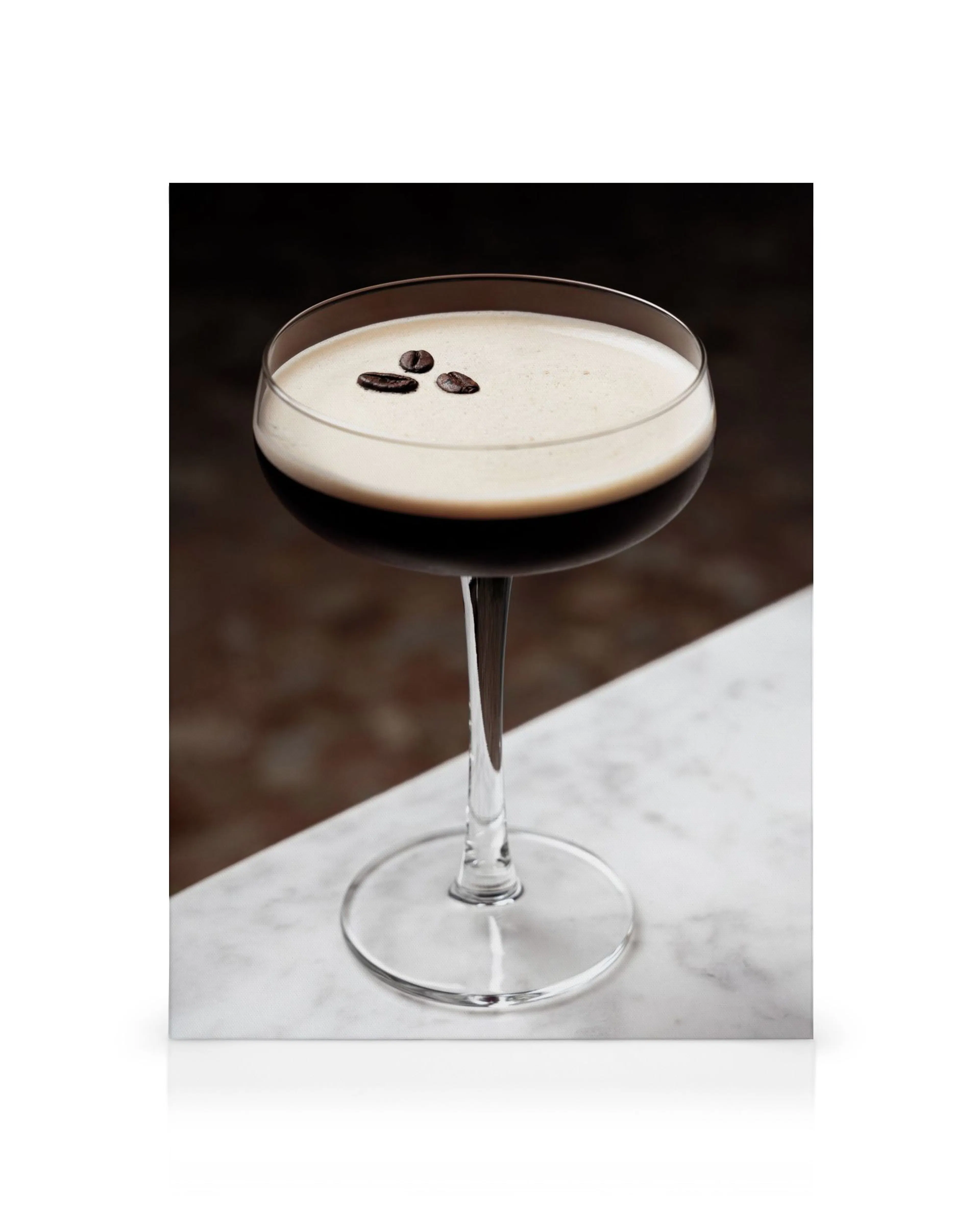 Martini-lasi tummalla kahvijuomalla ja vaalealla vaahdolla, jonka päällä on muutama kahvipapu. Juoma on valkoisella marmoripinna