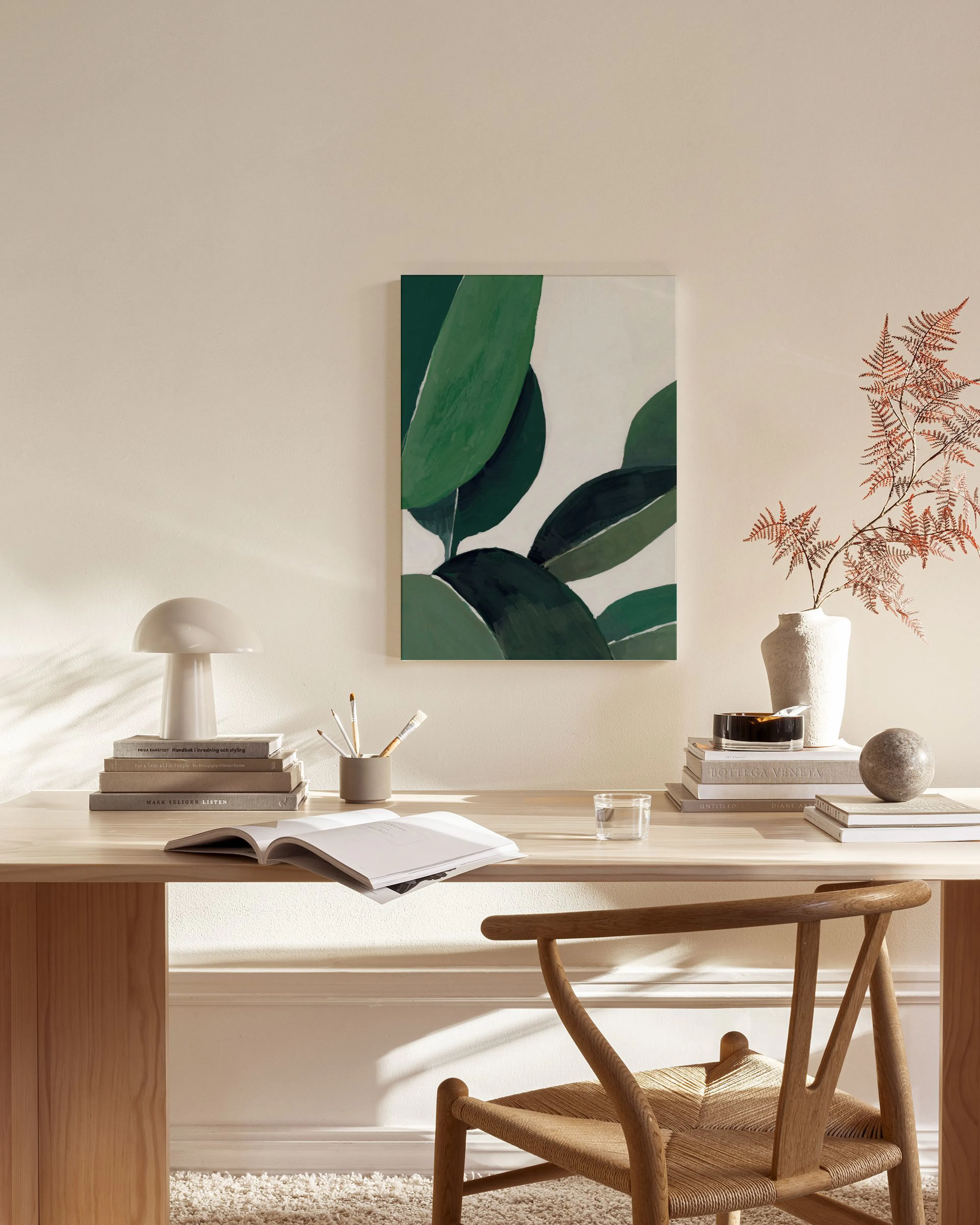 A canvas print of large green plant leaves on a white background, hanging in a bright, modern living room.