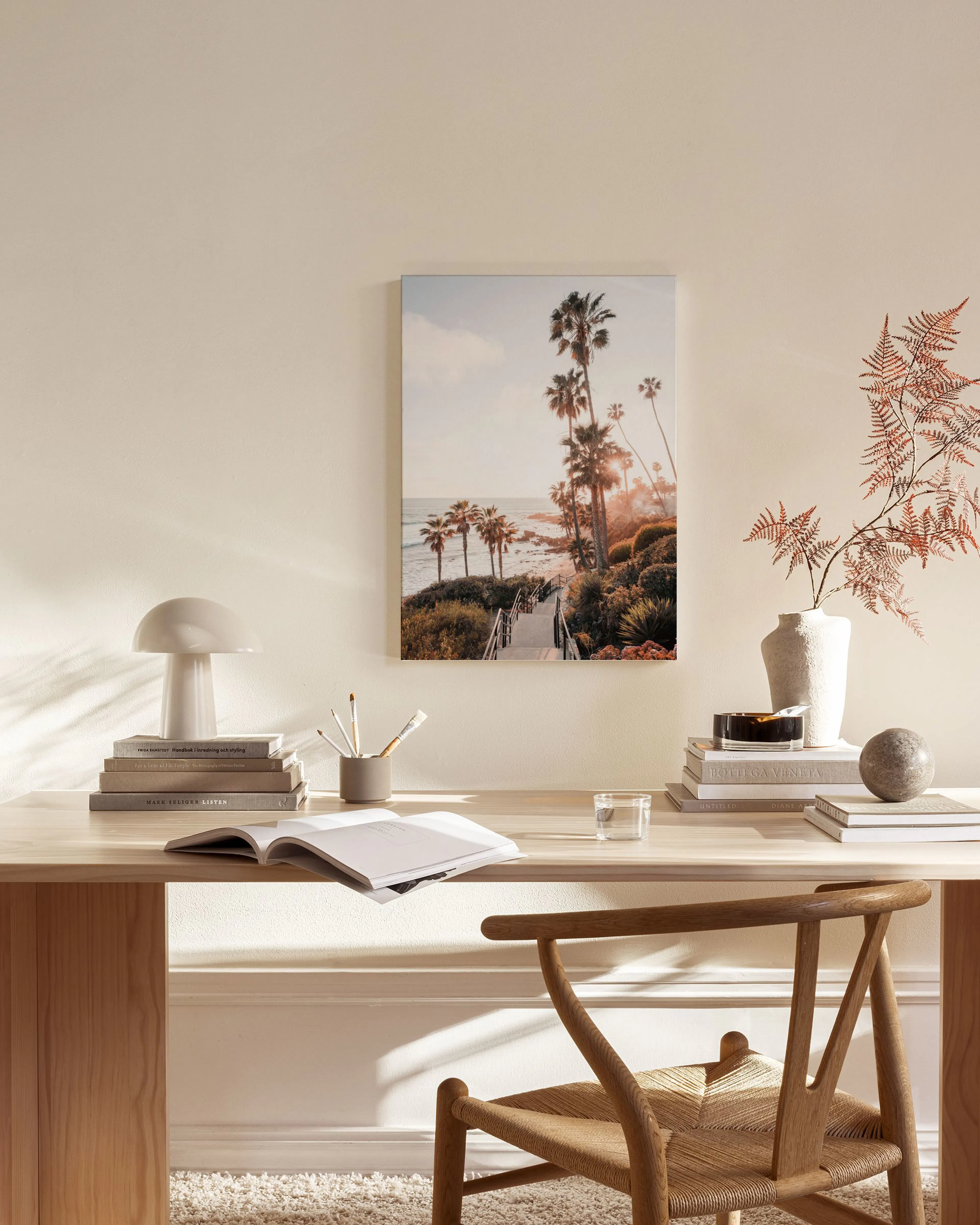 A coastal landscape canvas print of palm trees and ocean at sunset, displayed above a wooden bench in a cream-colored living roo