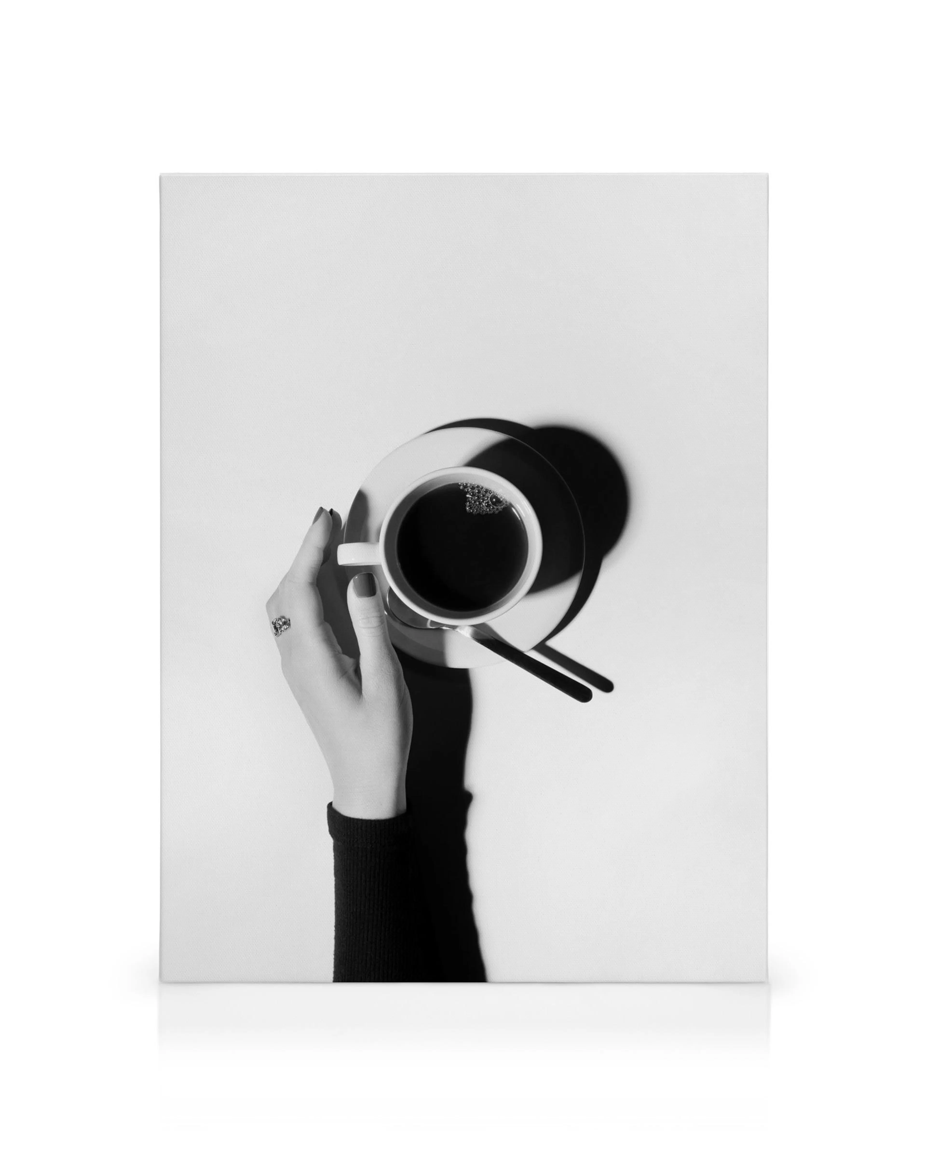 Mano sosteniendo taza de café blanco y negro con platillo y cucharas, arte de pared de cocina.