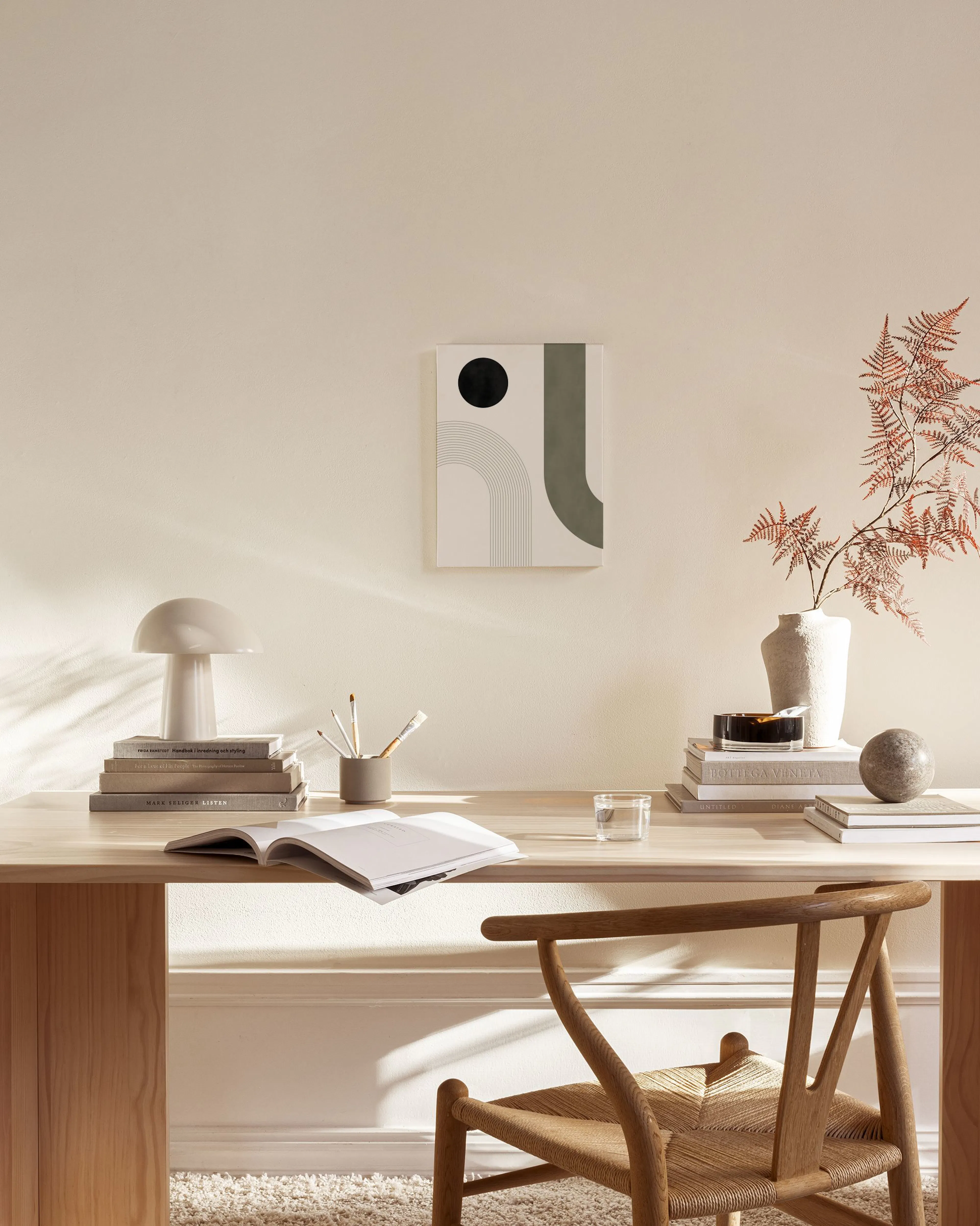 Canvas met zwarte cirkel en donkergroene golf, naast grijze bogen, hangend in een neutrale woonkamer.