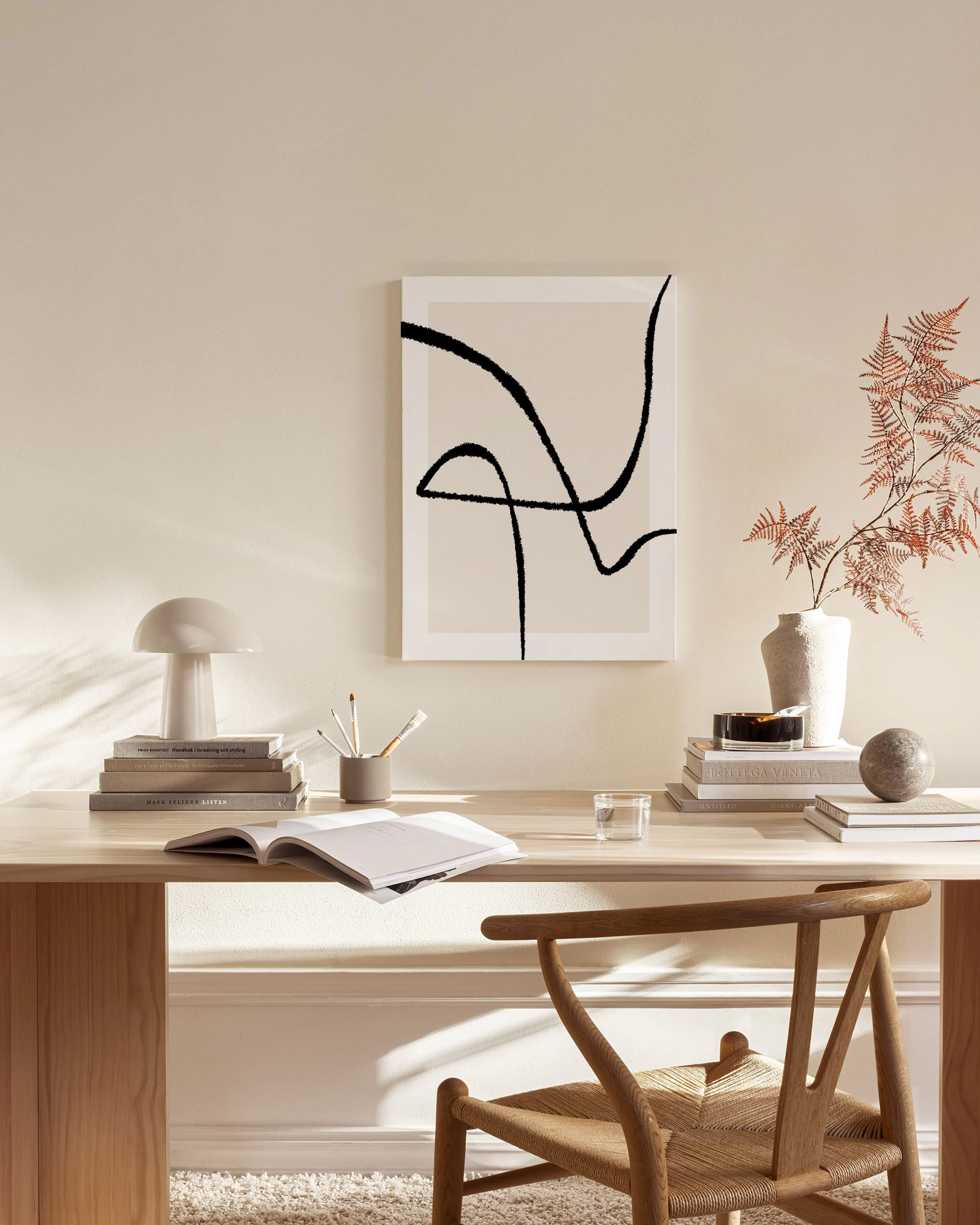 Canvastavla med svarta abstrakta linjer mot en ljusbeige bakgrund, hängande i ett ljust vardagsrum.