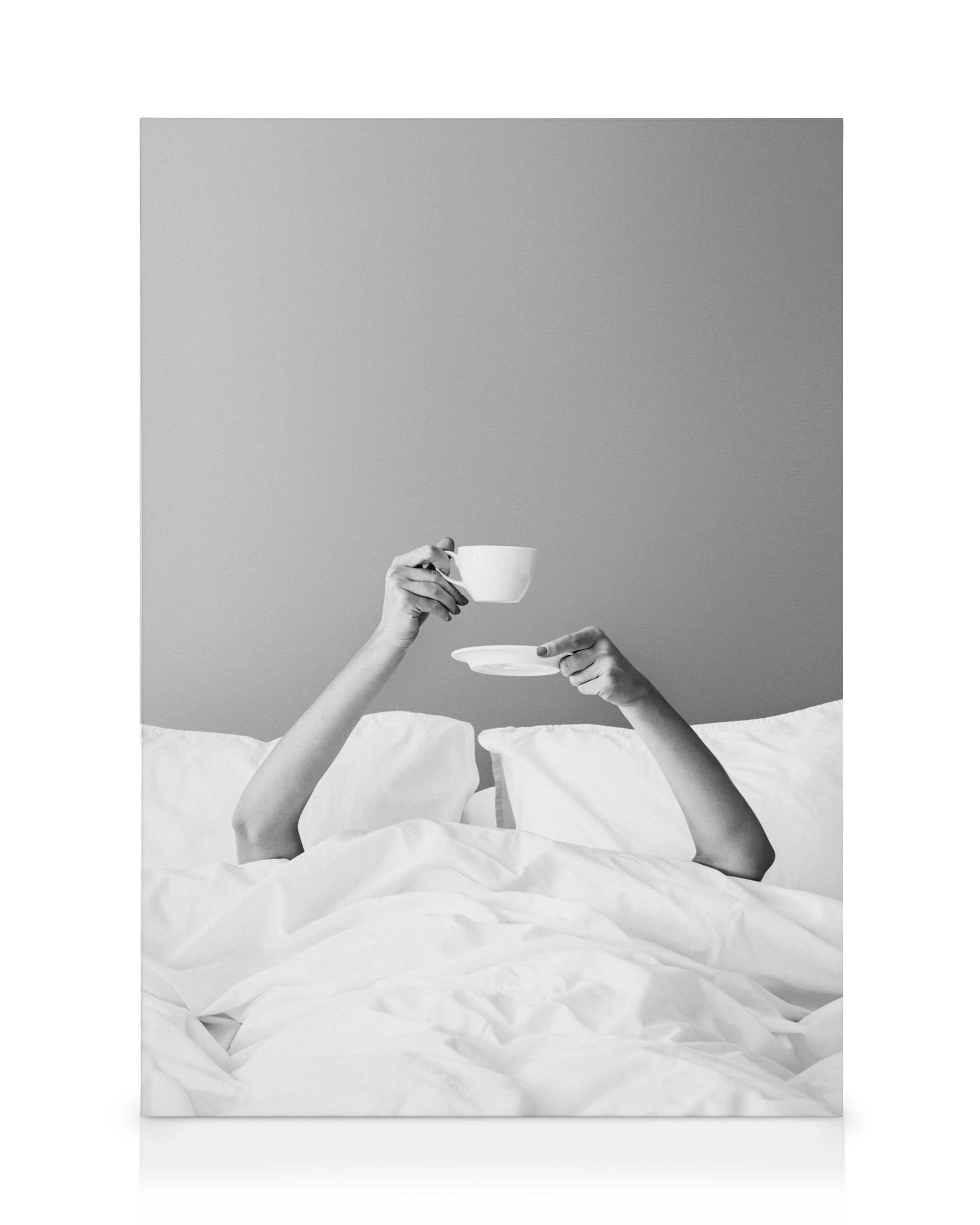 Schwarz-weißes Leinwandbild mit Armen, die eine Tasse und Untertasse über einer Betdecke halten, symbolisiert Frühstück im Bett.