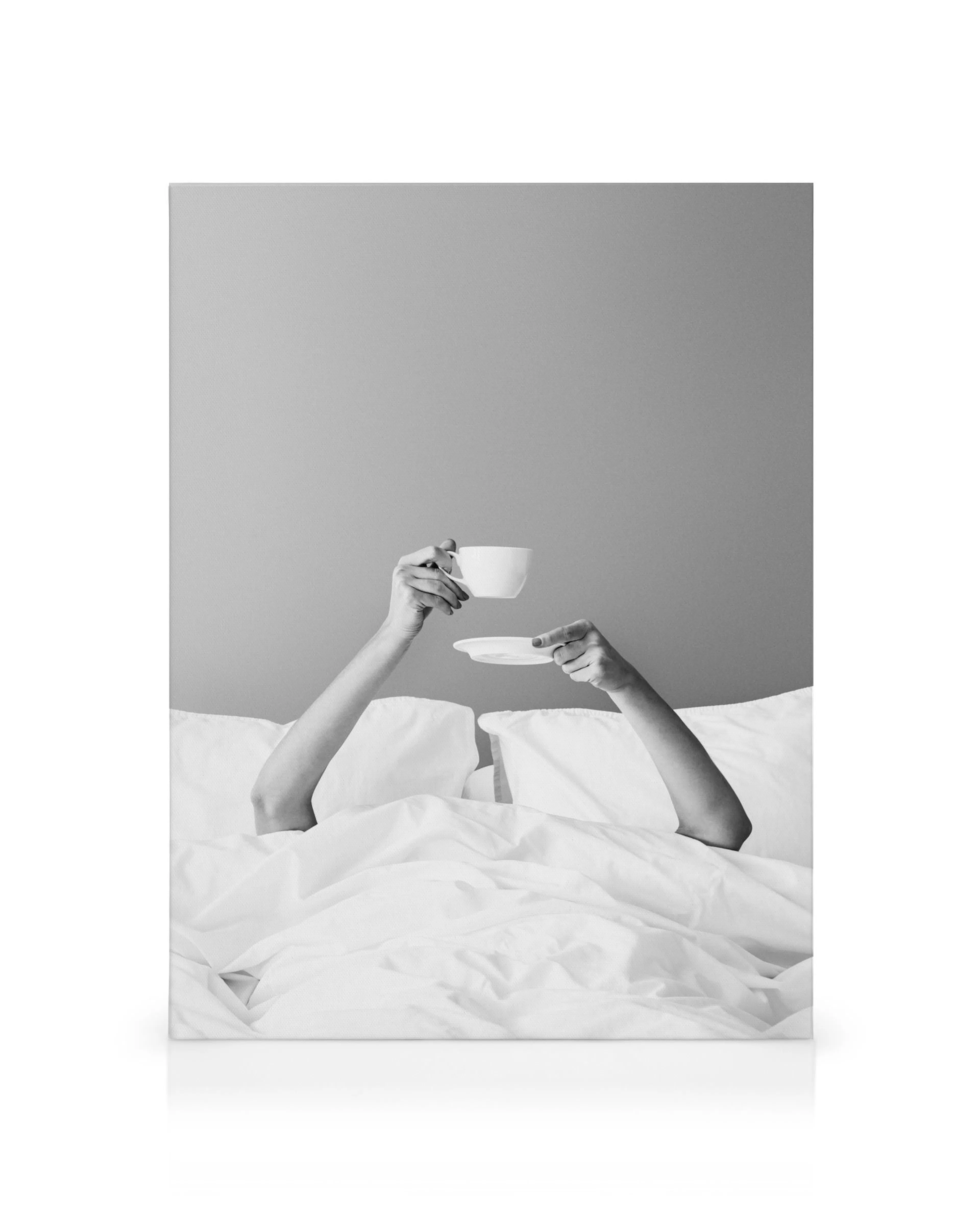 Lienzo monocromático: dos manos sosteniendo una taza y un platillo blancos sobre sábanas en la cama. Arte minimalista.