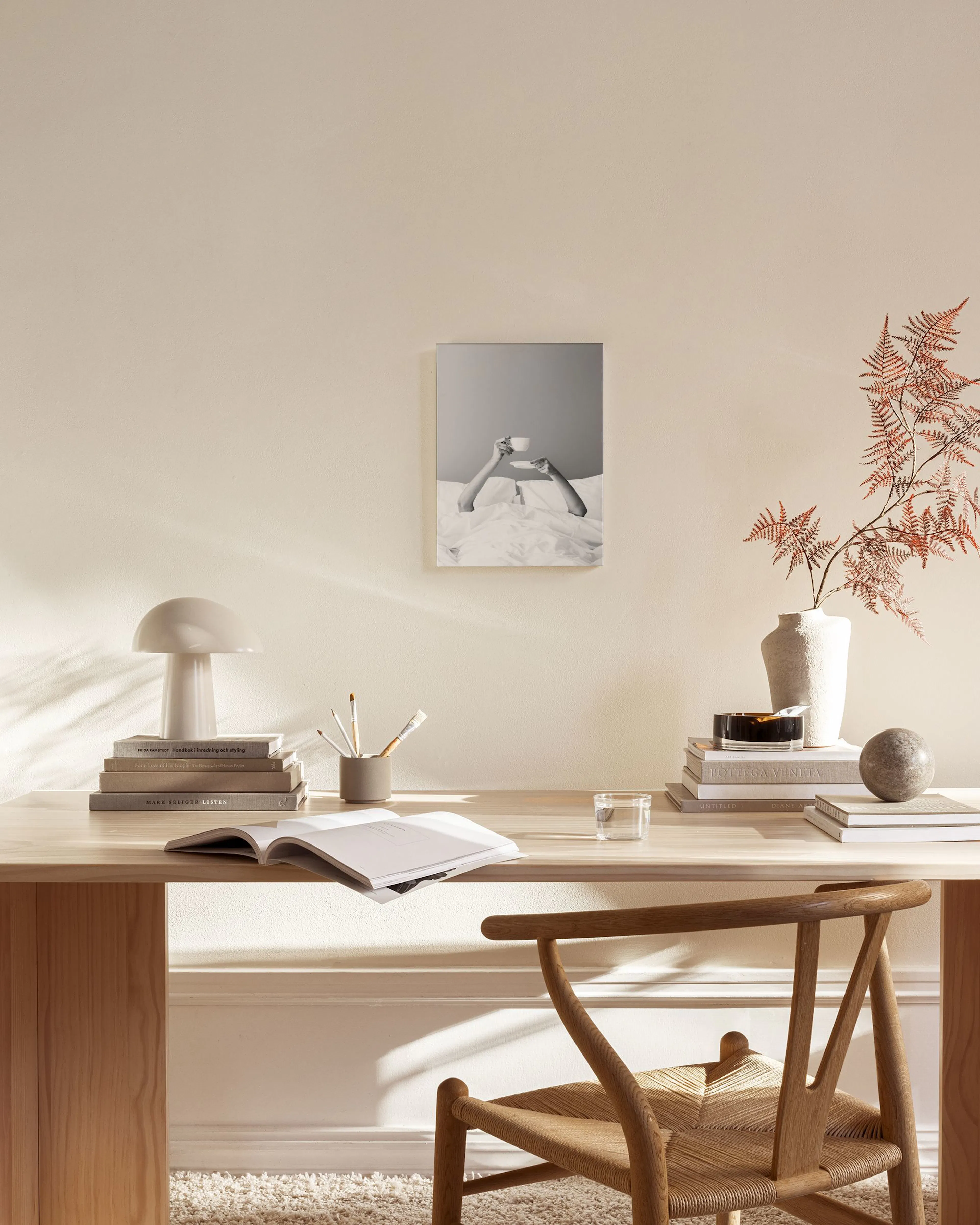 Lienzo monocromático de manos sosteniendo una taza de café en la cama, colgando en una sala minimalista con muebles de madera cl