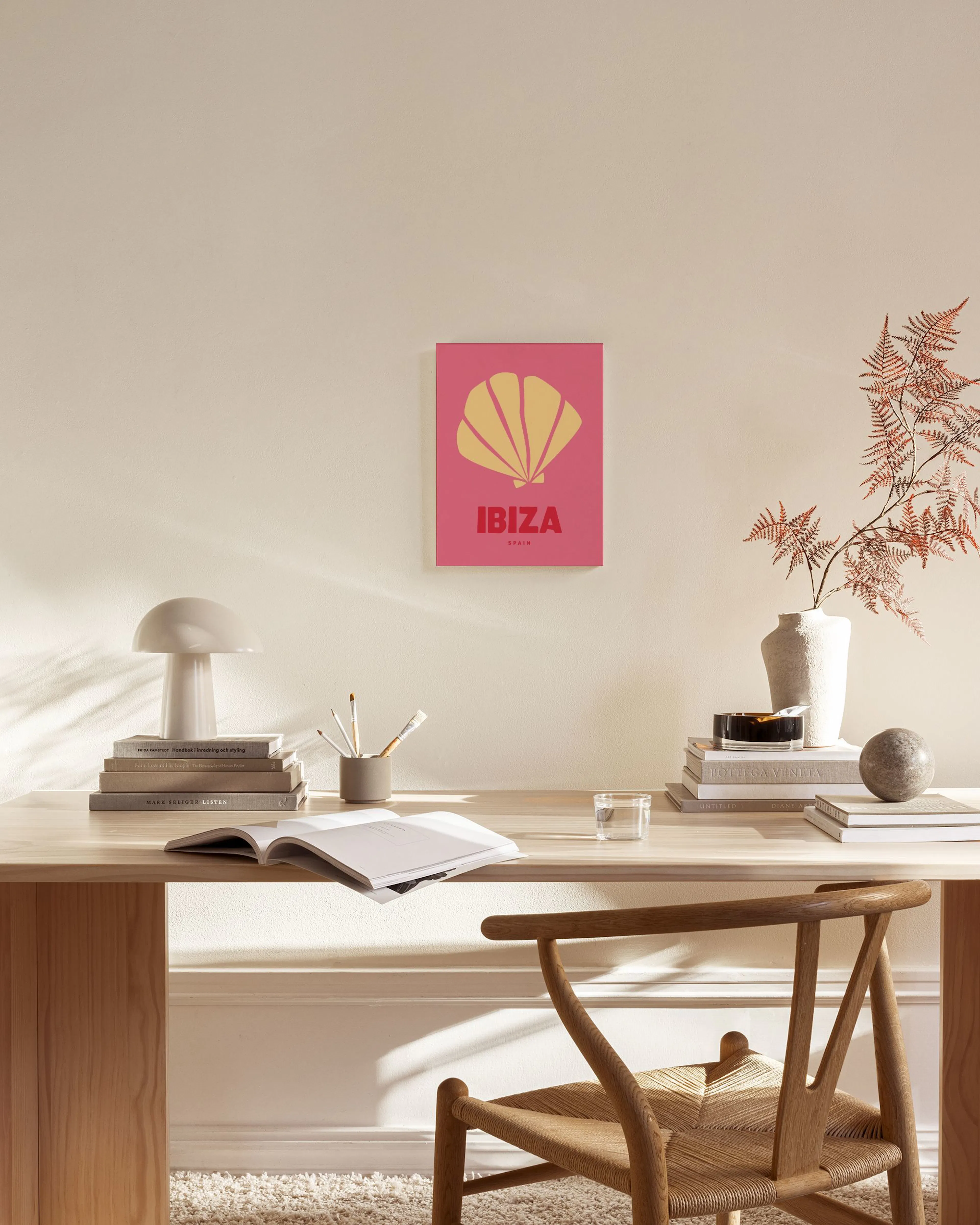 Een canvas met een geel schelpicoon op een roze achtergrond en de tekst IBIZA SPAIN, hangend in een moderne woonkamer.