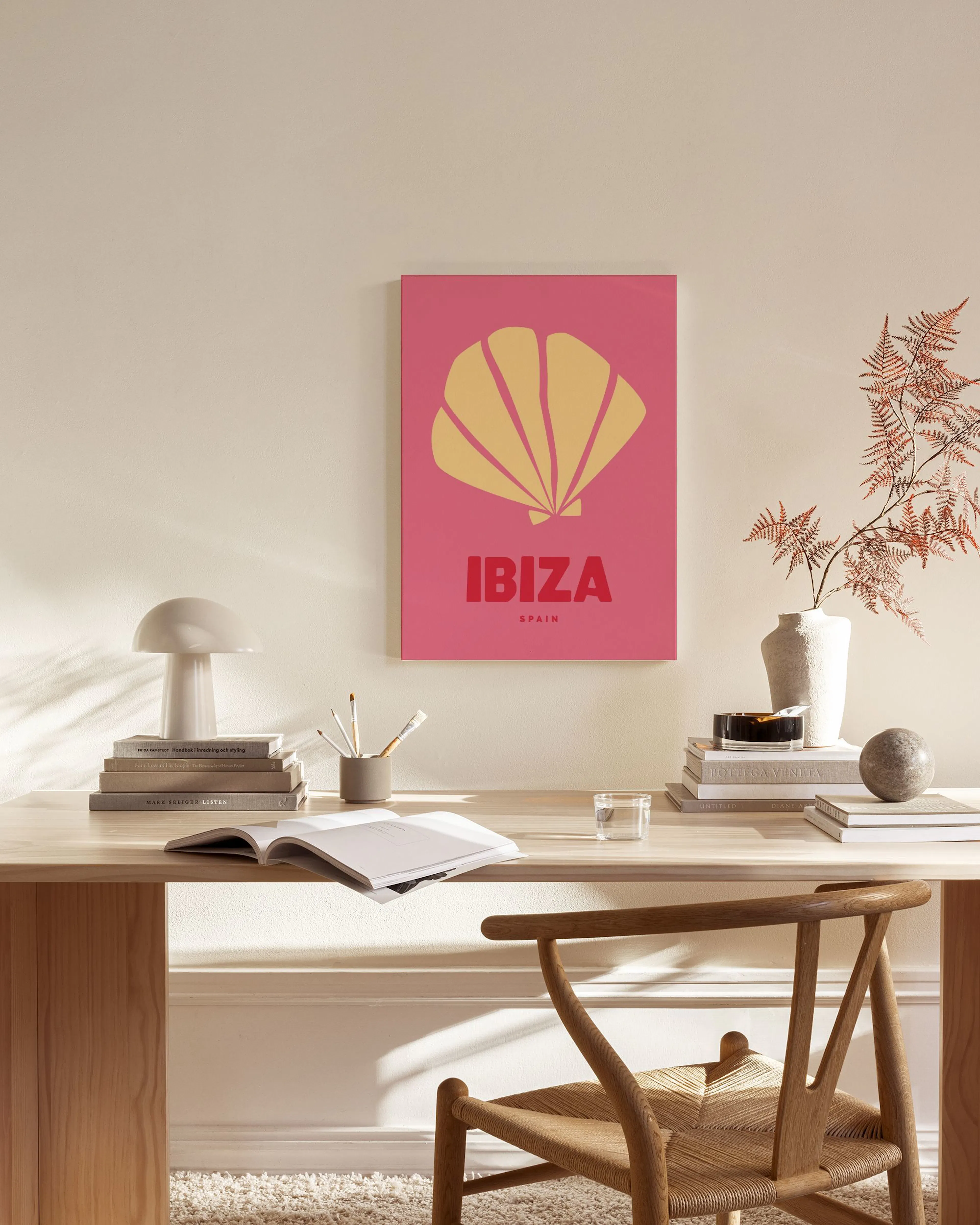 Toile de coquillage jaune sur fond rose avec le mot IBIZA, accrochée dans un salon lumineux au-dessus dun banc en bois.