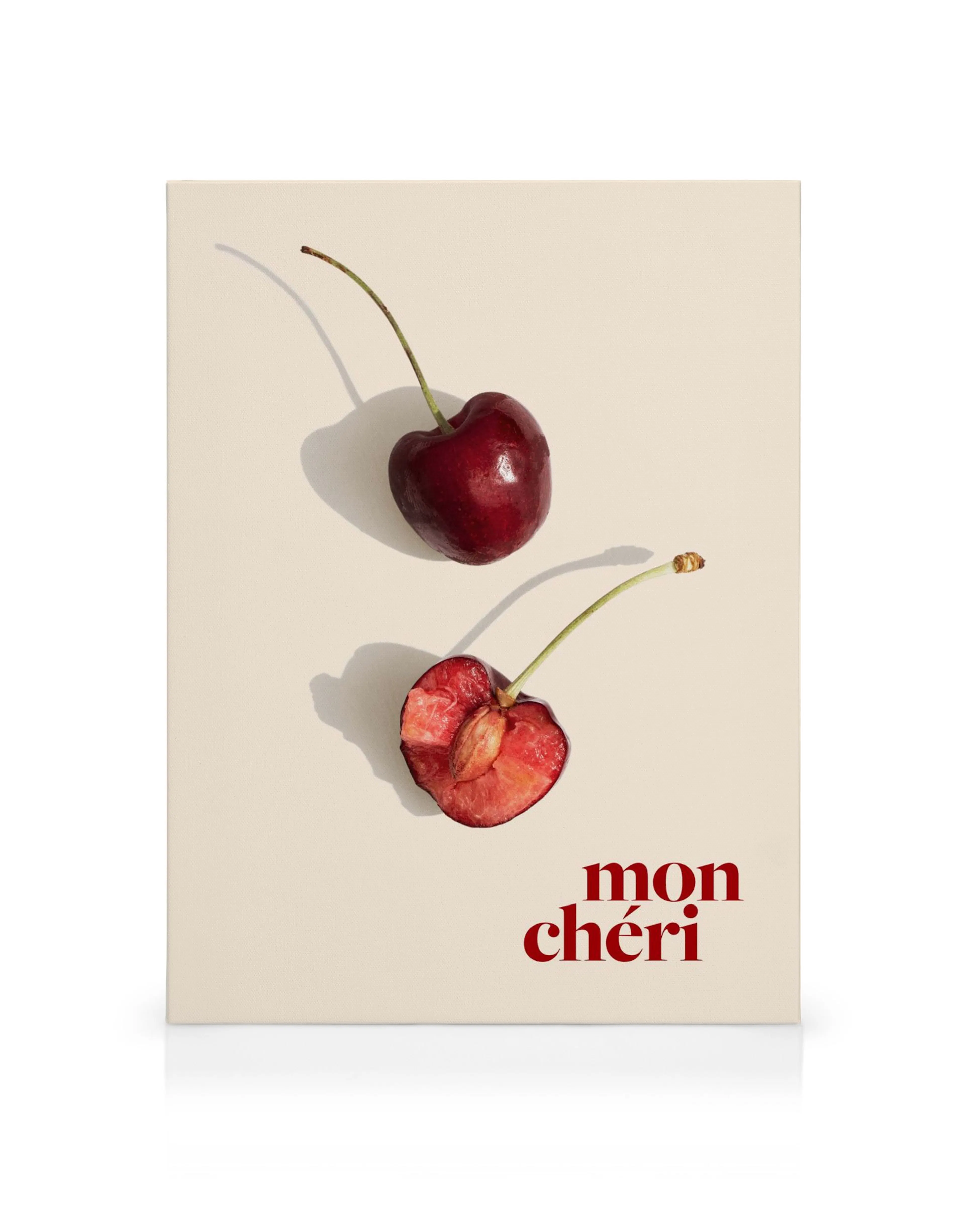 A canvas print featuring a whole red cherry and a half-cut cherry with mon chéri in red text on a cream background.