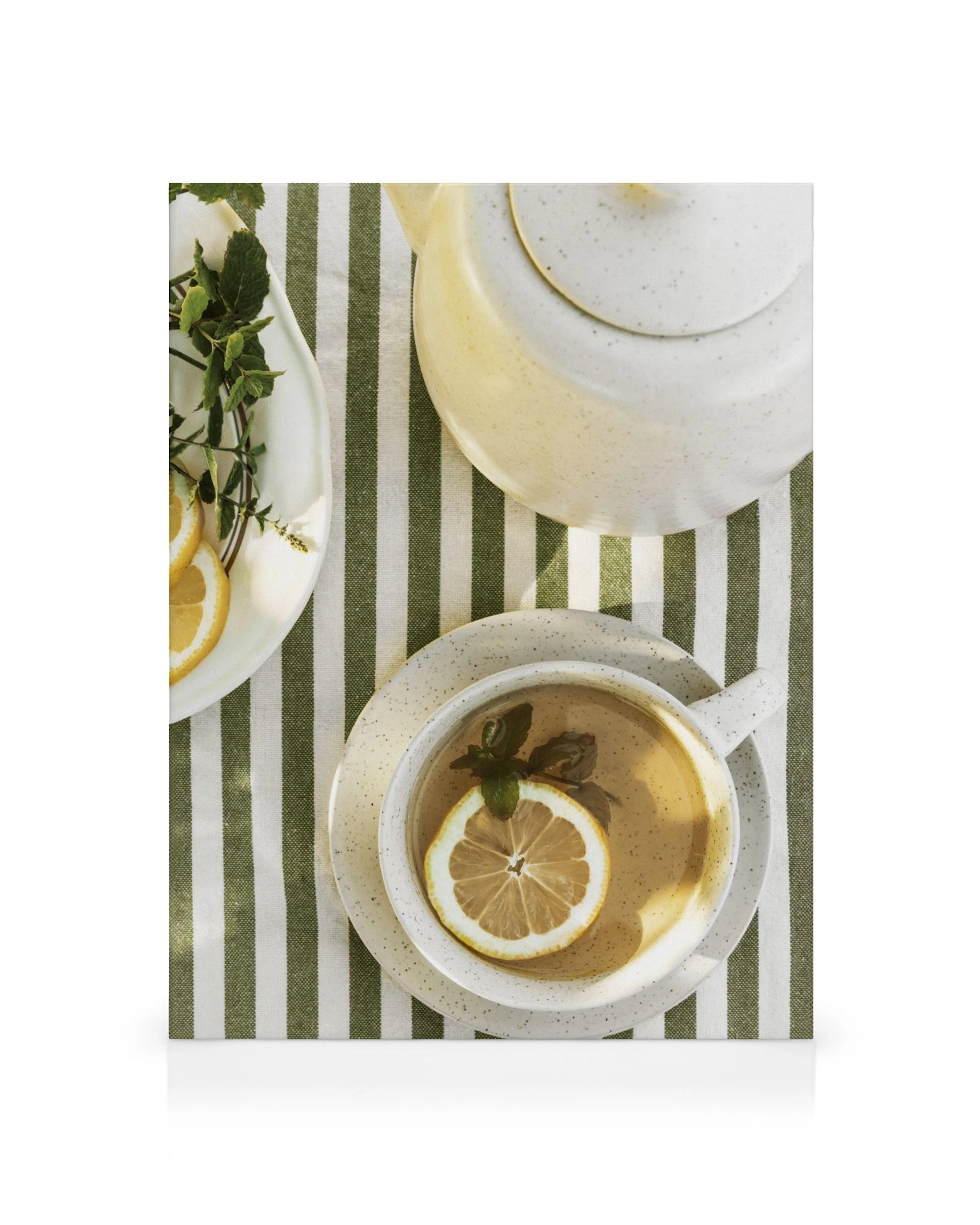 Toile dune tasse de thé avec citron et menthe sur une nappe rayée vert et blanc, à côté dune théière.
