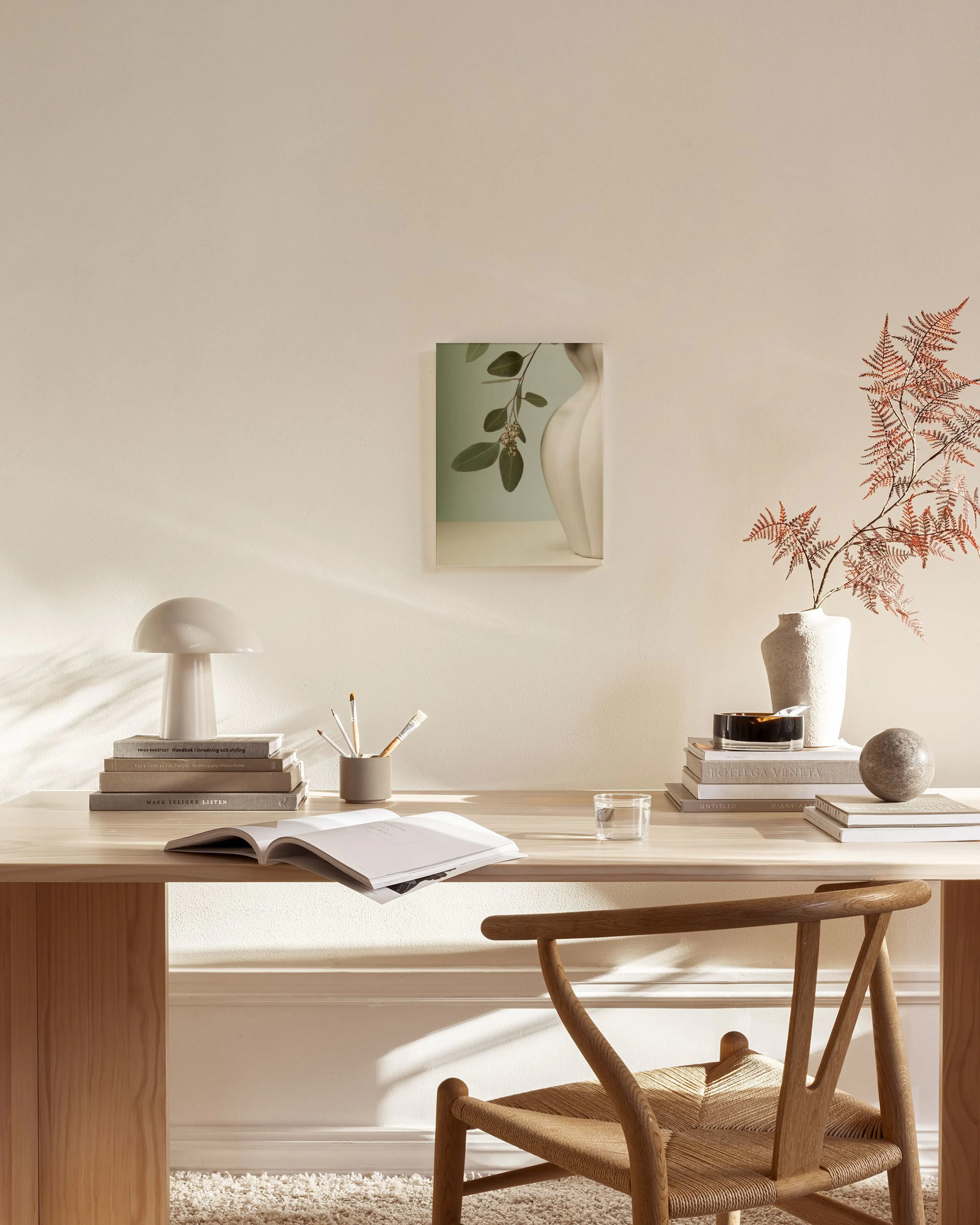 A canvas print featuring a light green branch with leaves and small buds, next to a cream-coloured fluted vase on a pale yellow 